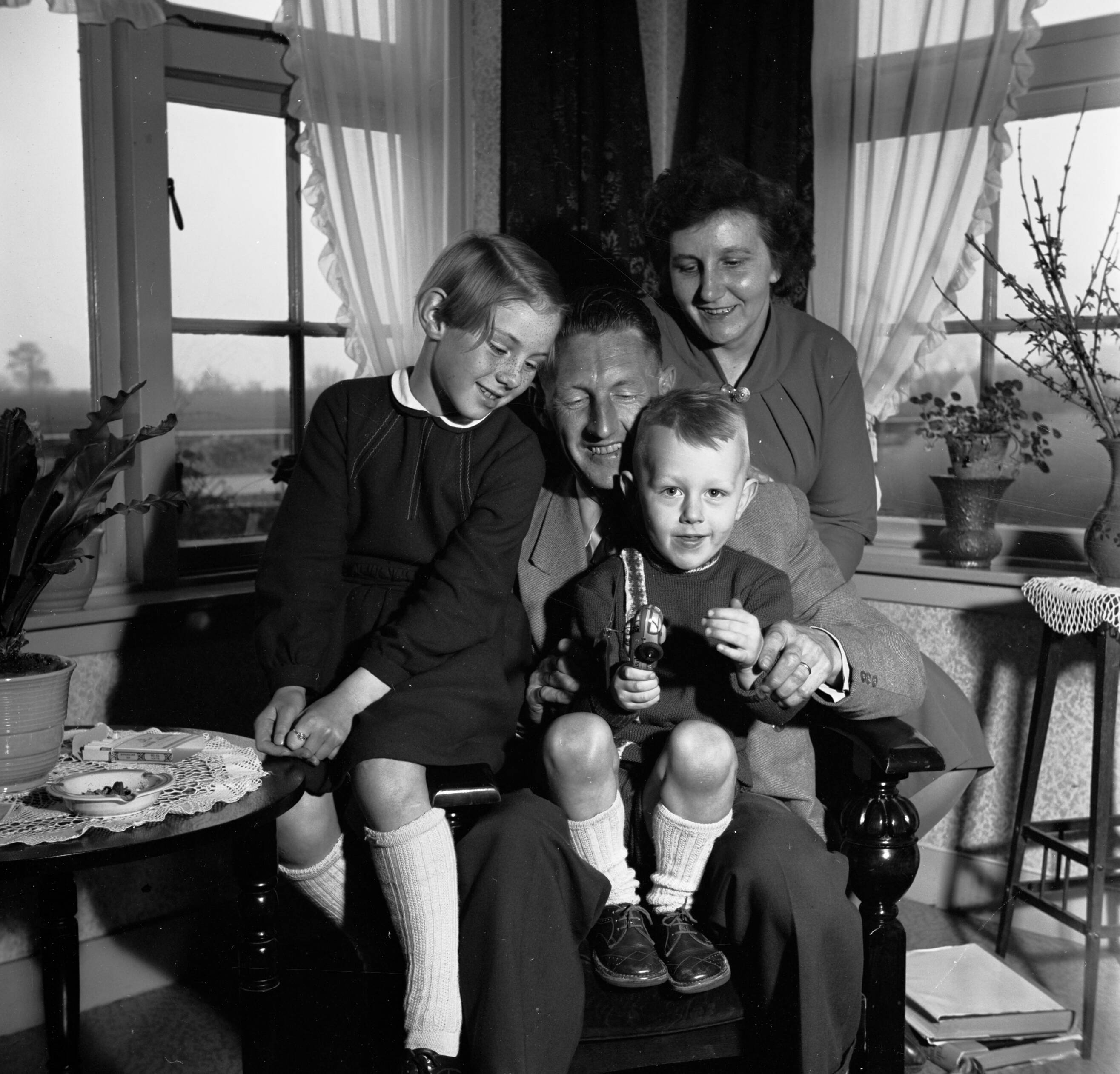 Fotocollectie Van de Poll — Gerard, zijn vrouw en hun beide kinderen in de huiskamer terwijl ze naar een stuk speelgoed kijken — Foto: Poll, Willem van de. Licentie: Set B: Rechtenvrij / Publiek Domein. Bron: Nationaal Archief. http://hdl.handle.net/10648/aeccd6aa-d0b4-102d-bcf8-003048976d84