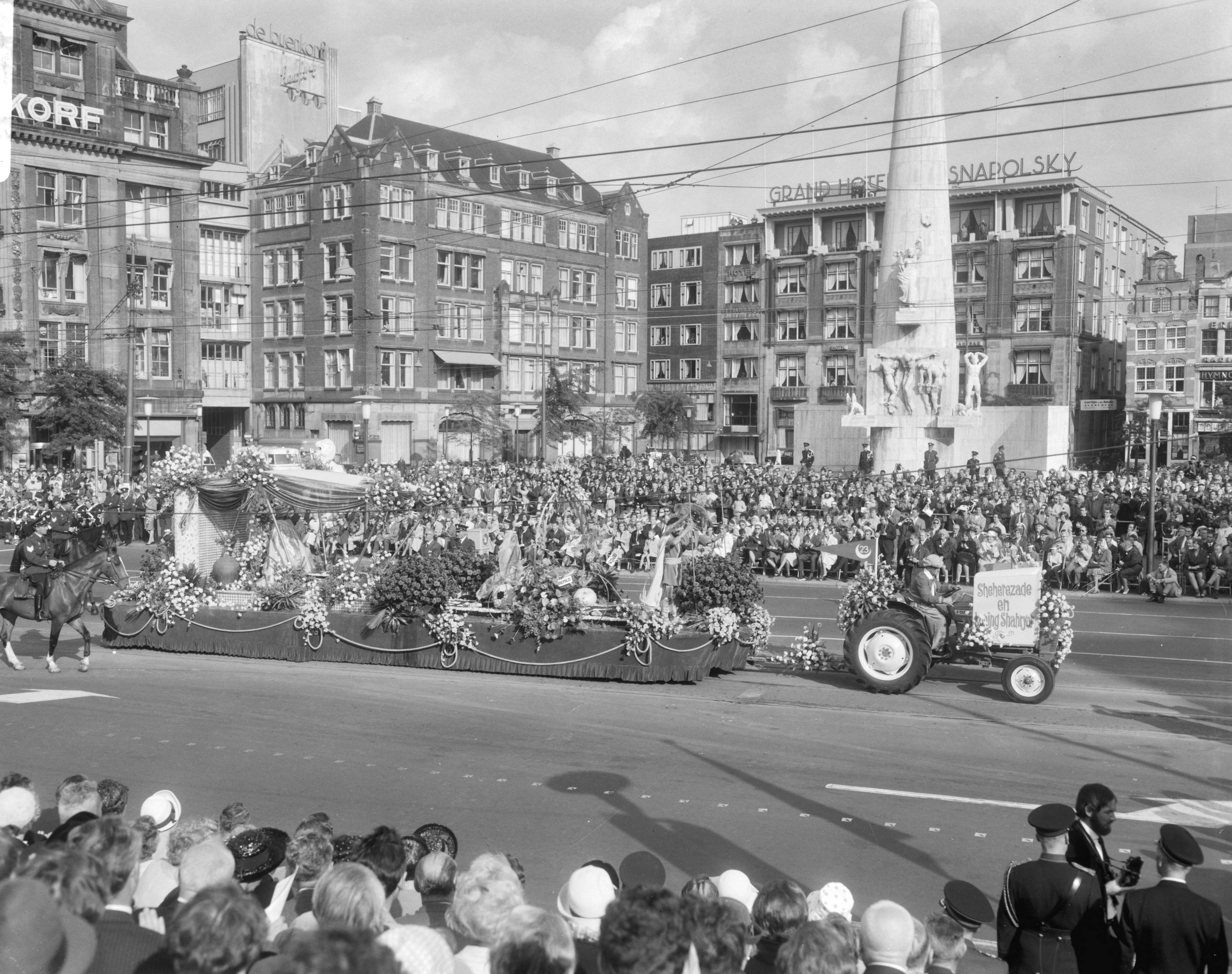 Bloemencorso van Aalsmeer te Amsterdam — Een praalwagen bij de Dam te Amsterdam met op de achtergrond het Nationaal Monument — Foto: Bilsen, Joop van / Anefo. Licentie: Set B: Rechtenvrij / Publiek Domein. Bron: Nationaal Archief. http://hdl.handle.net/10648/aafaeeea-d0b4-102d-bcf8-003048976d84