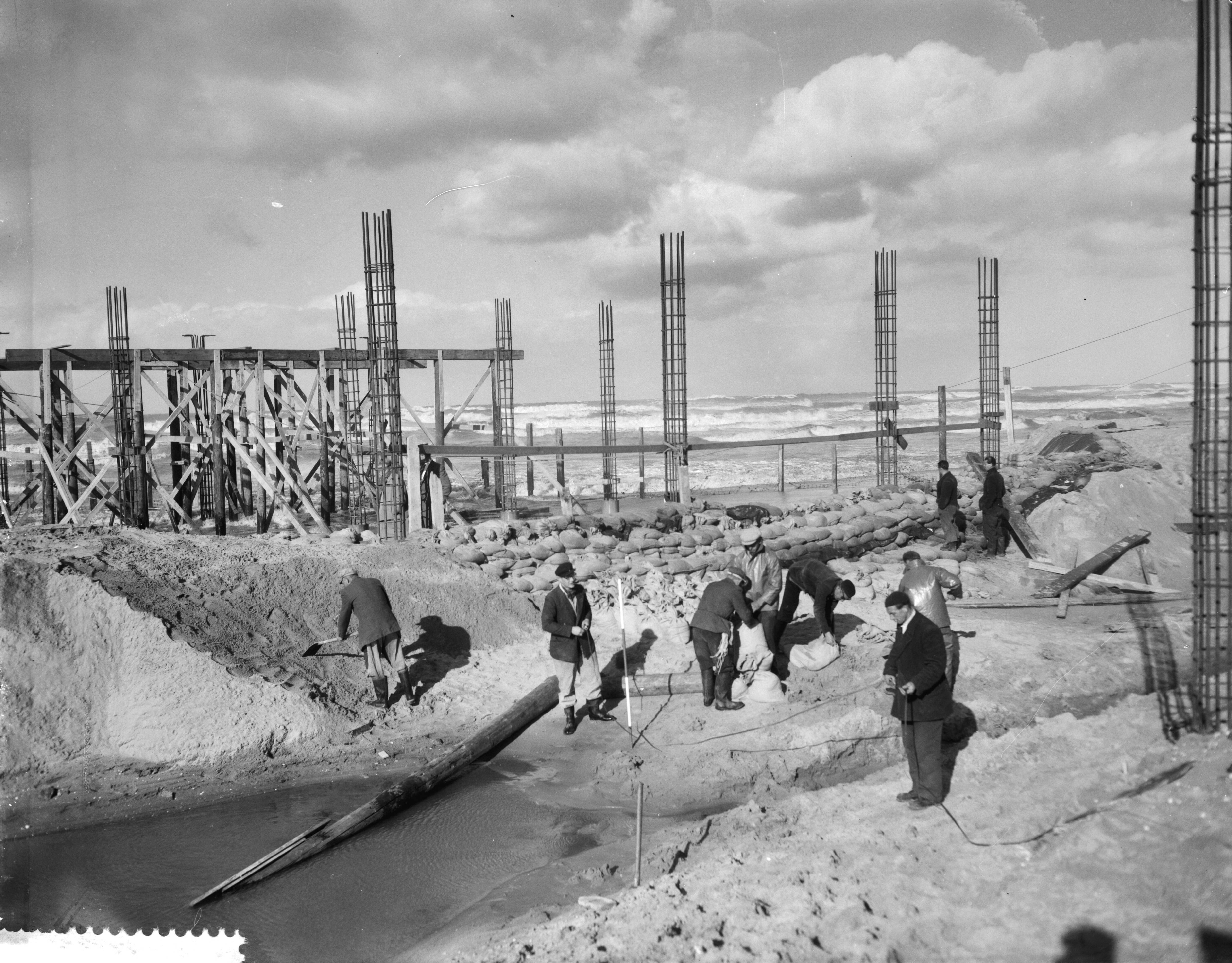 Fotocollectie Anefo — Bouw pier Scheveningen stagneert door storm. Dijkversterkingen met zandzakken — Foto: Bilsen, Joop van / Anefo. Licentie: Set B: Rechtenvrij / Publiek Domein. Bron: Nationaal Archief. http://hdl.handle.net/10648/a9a0c97a-d0b4-102d-bcf8-003048976d84