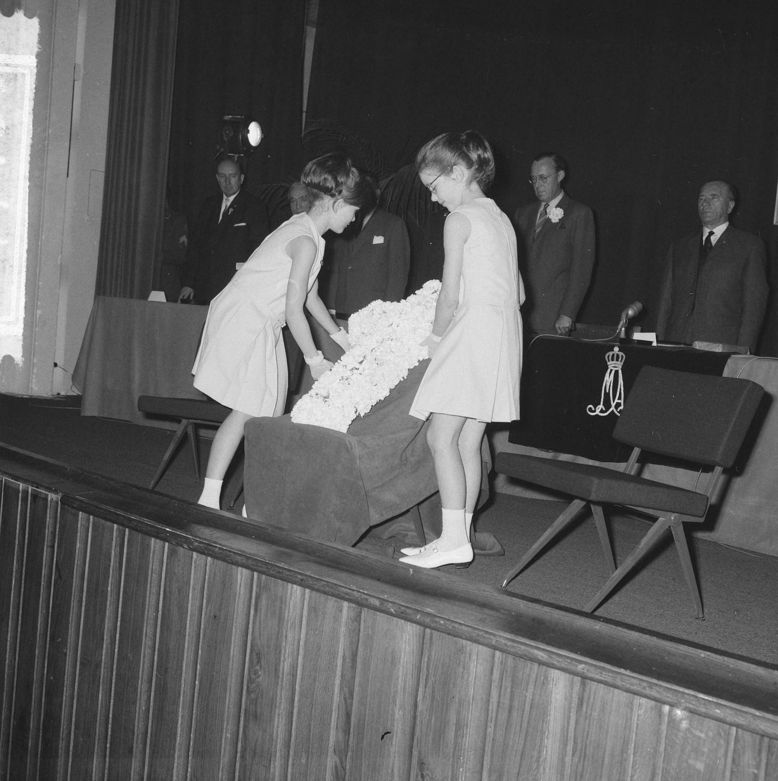 Fotocollectie Anefo — Bevrijdingscongres Nationale Federatie Raad van het Voormalig Verzet Nederland in de KMA te Breda, bijgewoond door prins Bernhard. Herdenking bij aanvang, twee meisjes plaatsen een kruis van witte anjers op een verhoging op het toneel — Foto: Nijs, Jac. de / Anefo. Licentie: Set B: Rechtenvrij / Publiek Domein. Bron: Nationaal Archief. http://hdl.handle.net/10648/aaa5c8ca-d0b4-102d-bcf8-003048976d84