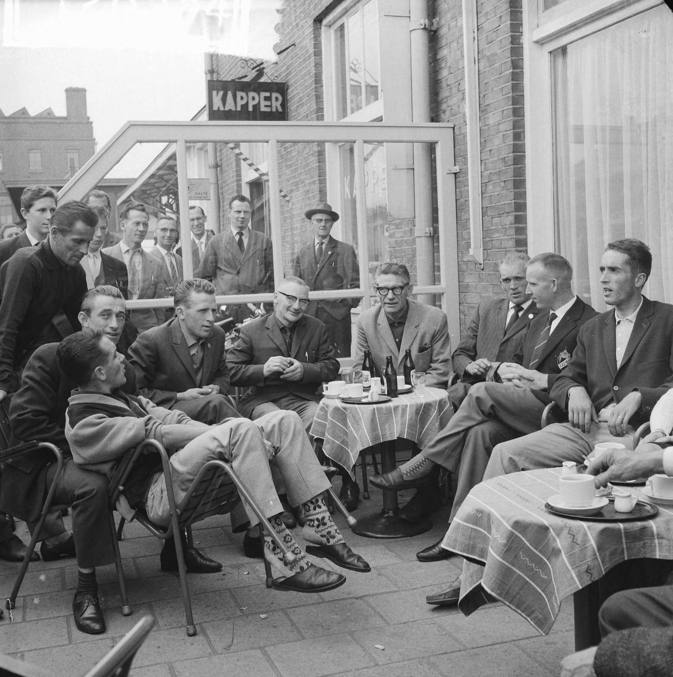 Tour de France 1961 — Vertrek Tour de France ploeg naar Frankrijk. De renners en officials op het terras. Zittend vlnr. Piet Damen, Wout Wagtmans, Jaap Kersten, verzorger, ploegleider Klaas Buchly, Coen Niesten, Piet van Est en Ab Geldermans — Foto: Koch, Eric / Anefo. Licentie: Set B: Rechtenvrij / Publiek Domein. Bron: Nationaal Archief. http://hdl.handle.net/10648/a9d9a286-d0b4-102d-bcf8-003048976d84