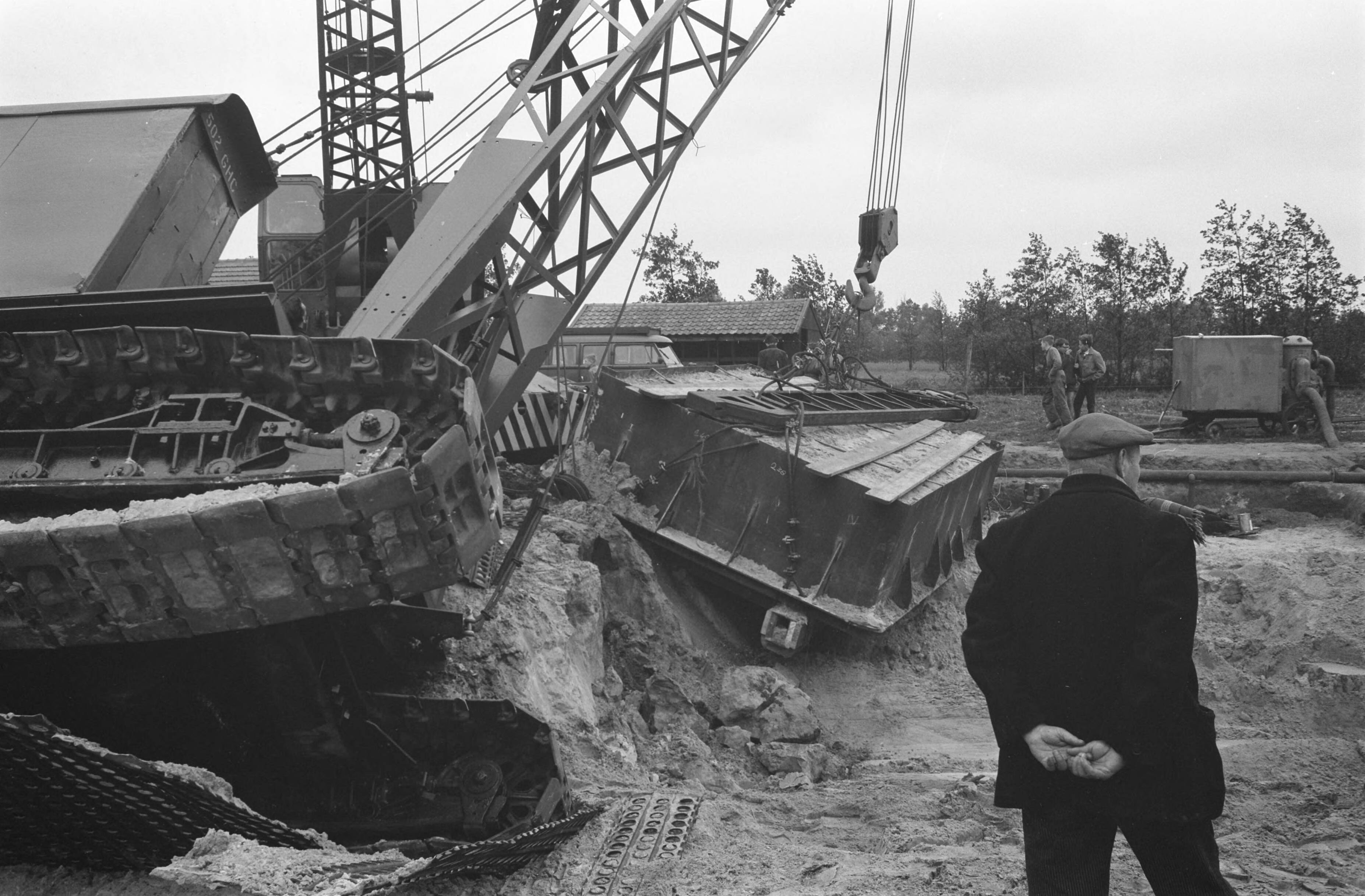 Fotocollectie Anefo — In Esch (N.B.) zijn militairen van het depot Genietroepen van de Koning Willem I-kazerne in Den Bosch bezig geweest met het uitgraven van een Romeins graf uit het begin van onze jaartelling. Het graf werd in een metalen bekisting gebouwd om in zijn geheel naar Amersfoort te worden overgebracht, waar de Rijksdienst voor Oudheidkundig Bodemonderzoek het zal bestuderen. Gisteren wilden twee kranen het graf op een vrachtauto tillen; een van de kranen kantelde echter. Het graf bleef ongedeerd — Foto: Pot, Harry / Anefo. Licentie: Set B: Rechtenvrij / Publiek Domein. Bron: Nationaal Archief. http://hdl.handle.net/10648/a9d66620-d0b4-102d-bcf8-003048976d84