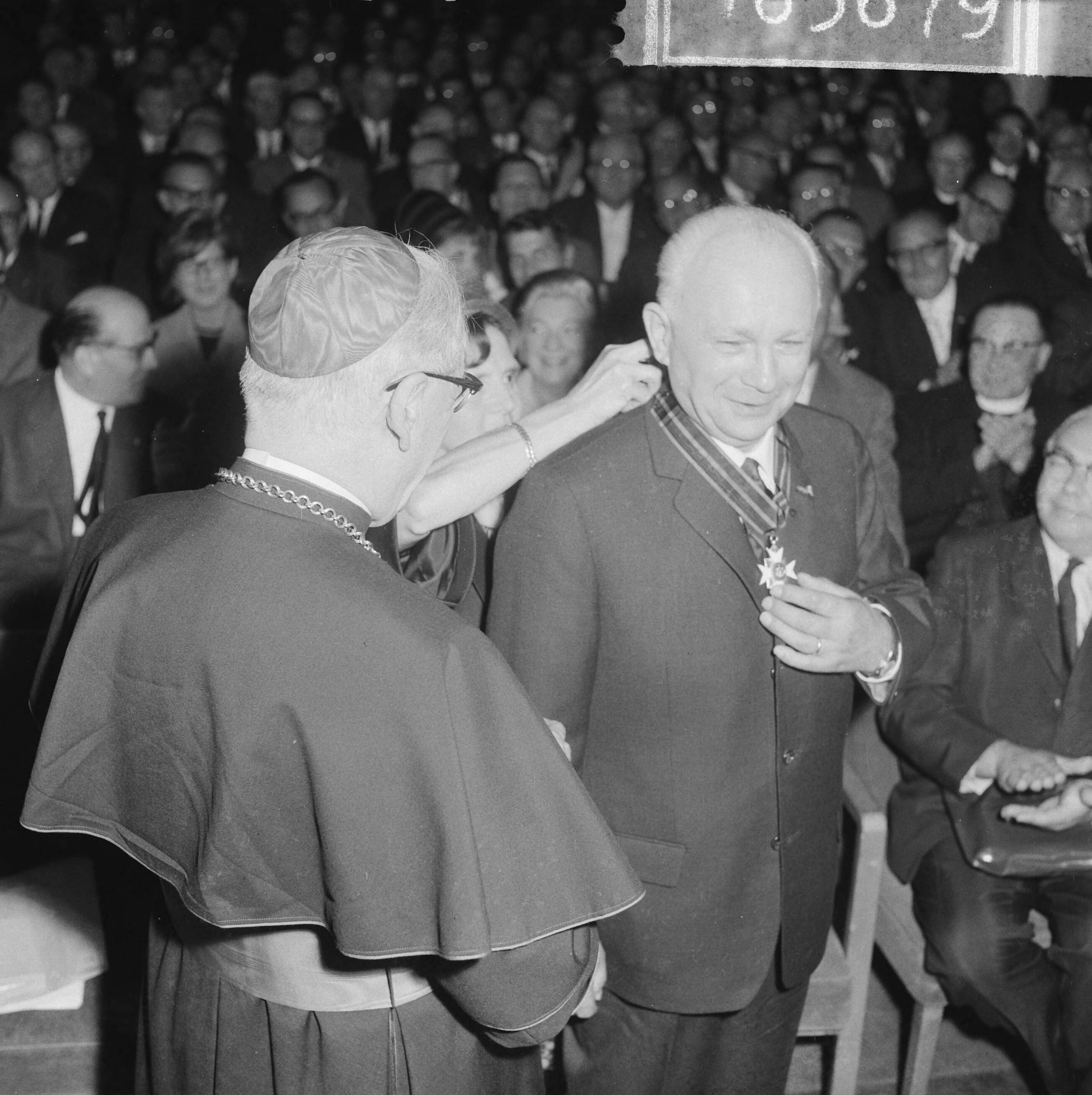 Fotocollectie Anefo — De voormalige voorzitter van het NKV [K.A.B.], J.A. Middelhuis, heeft afscheid genomen tijdens een receptie in de Utrechtse Stadsschouwburg. Kardinaal Alfrink deelde hem de versierselen uit die behoren bij het commandeurschap in de Orde van Sint Silvestre, aan Middelhuis verleend door paus Johannes XXIII, mevrouw Middelhuis schikt de decoratie van haar man — Foto: Gelderen, Hugo van / Anefo. Licentie: Set B: Rechtenvrij / Publiek Domein. Bron: Nationaal Archief. http://hdl.handle.net/10648/aa6df788-d0b4-102d-bcf8-003048976d84