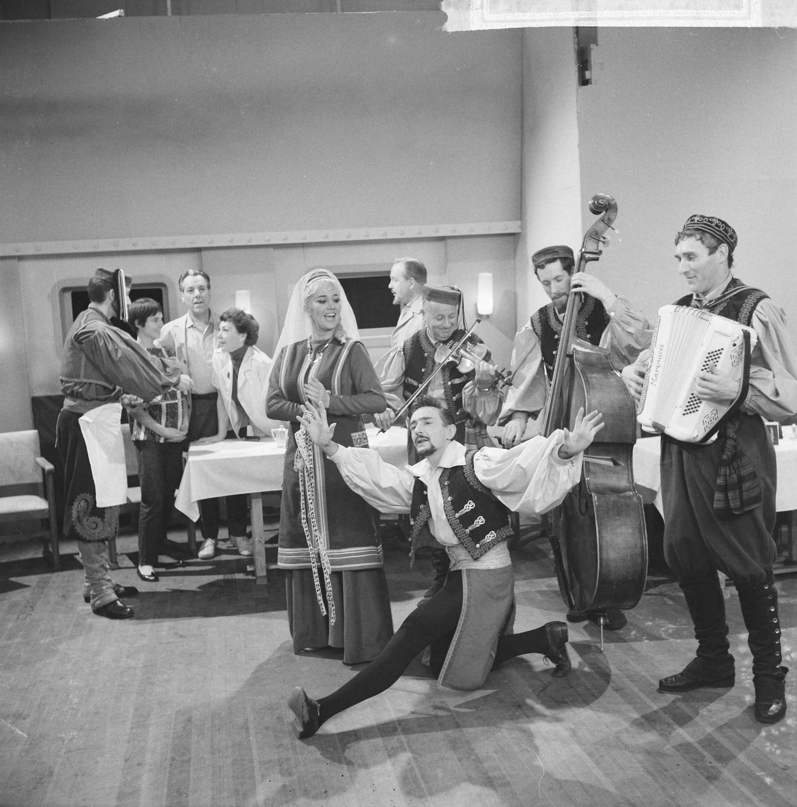 Fotocollectie Anefo — Opname televisiespel "Met 24 pk door Europa" (uitzending niet doorgegaan). De Spaanse Nederlander Marino en zijn danspartner Antonia, met begeleiders. In de achtergrond vlnr. Simone Rooskens, Ko van Dijk, Teddy Schaank en Guus Verstraete jr.Negatieven zijn een jaar later, op 31-3-1964, geregistreerd in fotoadministratie Anefo! Deze aflevering is wél uitgezonden, als eerste op 20-10-1963. Op 22-11-1963 schrijft Trouw: Er komen geen afleveringen meer van de televisiestrip "Met 24 P.K. door Europa" met Ko van Dijk, Teddy Schaank en Simone Rooskens. De AVRO heeft besloten de serie te staken. Reden: de strip kon ook na bewerking van het oorspronkelijke script niet aan de gestelde eisen voldoen. Karel Prior, hoofd amusementsprogramma's van de AVRO zei van deze door het echtpaar Mazure geschreven strip, dat ze „te filmisch" waren geschreven, waardoor men er in de televisiestudio's niet goed mee uit de voeten kon. Ellen en Georges Mazure, die zes afleveringen van hun stri