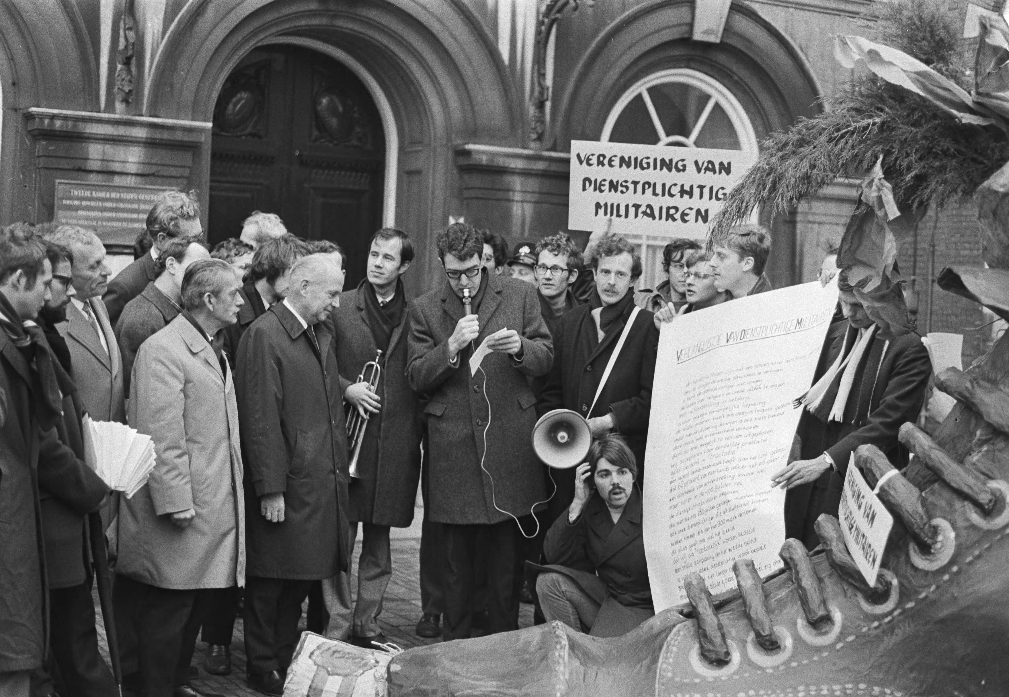Fotocollectie Anefo — Vereniging van dienstplichtige militairen biedt schoen met verlanglijst aan aan leden Tweede Kamer , Binnenhof, Den Haag — Foto: Evers, Joost / Anefo. Licentie: Set B: Rechtenvrij / Publiek Domein. Bron: Nationaal Archief. http://hdl.handle.net/10648/abac1508-d0b4-102d-bcf8-003048976d84