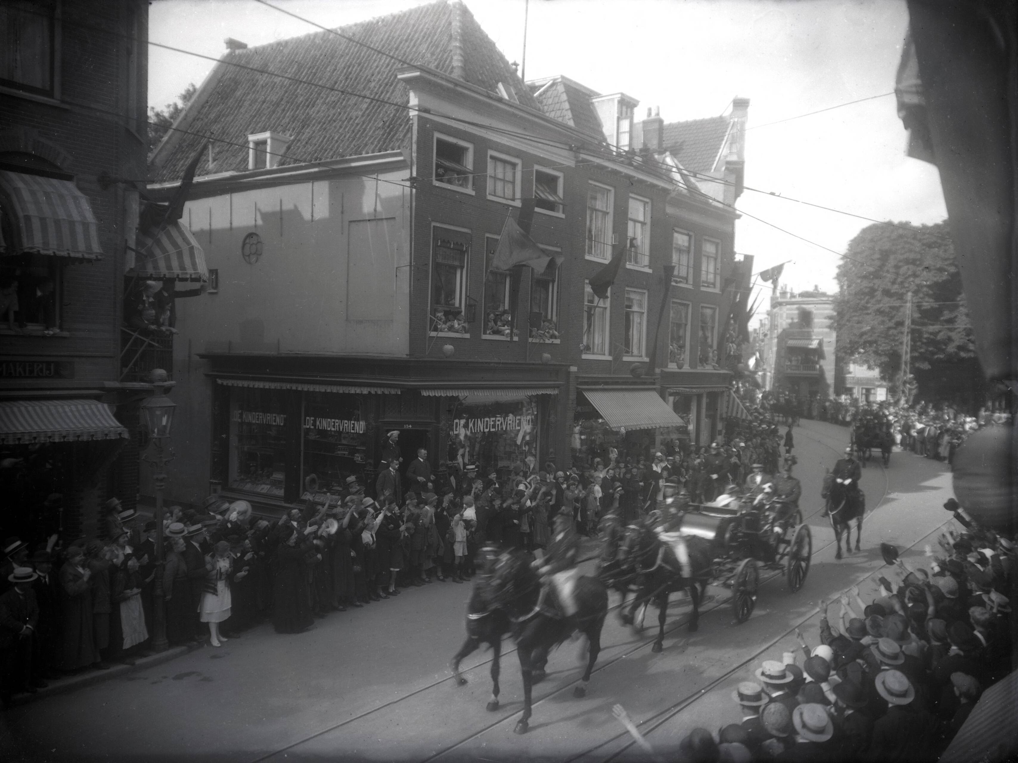"Royals, vorstenhuizen", Personen op naam — Grote Houtstraat richting Proveniershof met links de Kerkstraatrichting Gedempte Oude Gracht. Haarlem, Nederland, zonder datum [omstreeks 1920; de koninklijke familie (koningin Wilhelmina, prins Hendrik en kroonprinses Juliana (met witte hoed) maakt een rijtoer per koets door de stad. Het publiek staat juichend aan de kant.]. — Foto: Berg, Th.C.J. van den / Spaarnestad Photo (05887). Licentie: Set B: Rechtenvrij / Publiek Domein. Bron: Nationaal Archief. http://hdl.handle.net/10648/35429da6-760e-a382-e063-6df0900a6686