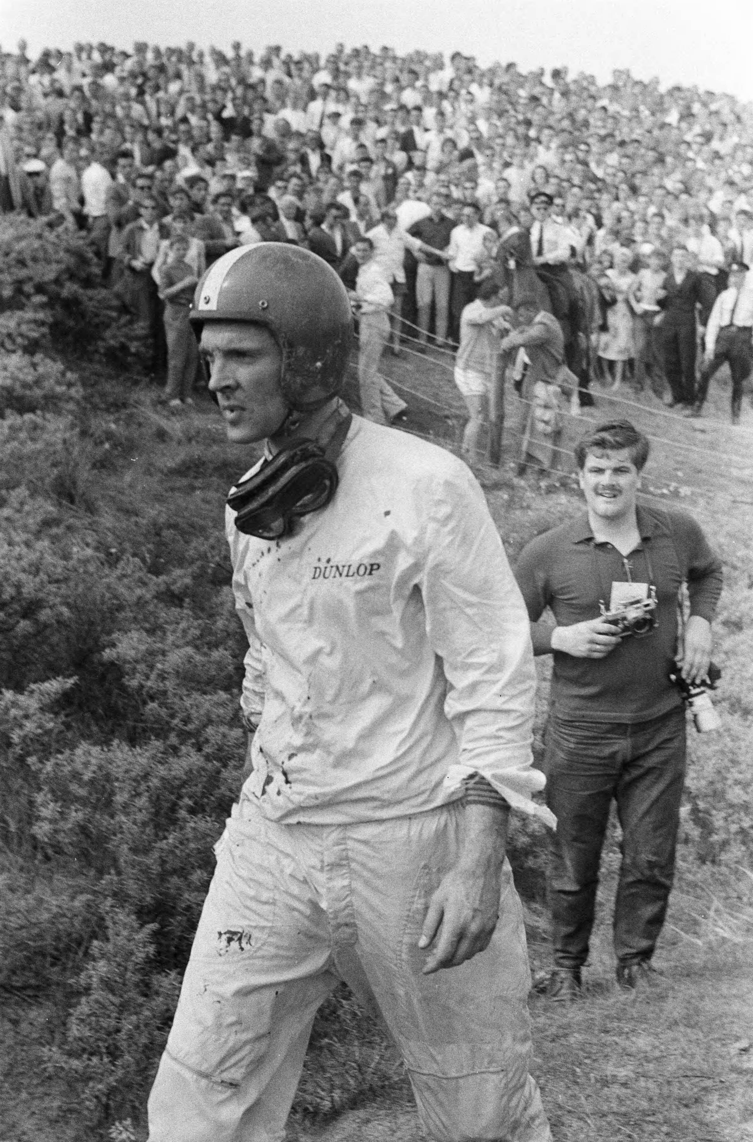 Autoraces op het circuit van Zandvoort. Dan Gurney wandelt terug naar de pits nadat hij in de Tarzanbocht rechtuit is gereden en over de hekken is gevlogen met zijn BRM F1 wagen door een defect aan de remmen. Hierbij kwam jammerlijk een jonge toeschouwer — Grote Prijs van Nederland op het circuit van Zandvoort. Dan Gurney wandelt terug naar de pits nadat hij in de Tarzanbocht rechtuit is gereden en over de hekken is gevlogen met zijn BRM F1 wagen door een defect aan de remmen. Hierbij kwam jammerlijk een jonge toeschouwer om het leven. — Foto: Fotograaf Onbekend / Anefo. Licentie: Set B: Rechtenvrij / Publiek Domein. Bron: Nationaal Archief. http://hdl.handle.net/10648/a9b11050-d0b4-102d-bcf8-003048976d84