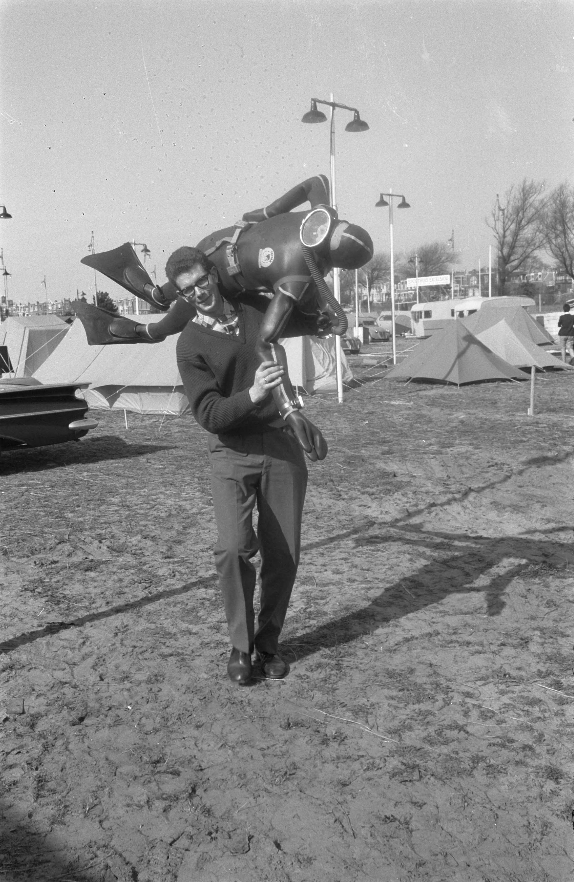 Fotocollectie Anefo — Inrichten tentoonstelling "Goed Kamp" in de Houtrusthal te Den Haag. Man loopt met pop aangekleed als duiker (kikvorsman) over buitenterrein — Foto: Pot, Harry / Anefo. Licentie: Set B: Rechtenvrij / Publiek Domein. Bron: Nationaal Archief. http://hdl.handle.net/10648/a9d00898-d0b4-102d-bcf8-003048976d84