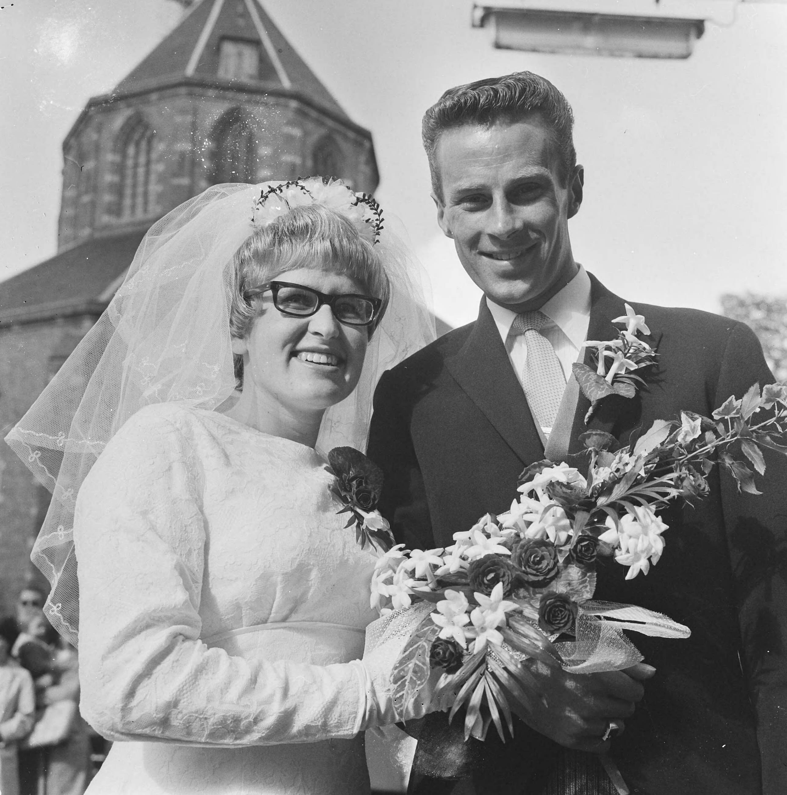 Zwemster Marianne Heemskerk en wielrenner Jaap Oudkerk treden in Naarden in het huwelijk — Het huwelijkspaar voor de kerk van Naarden — Foto: Evers, Joost / Anefo. Licentie: Set B: Rechtenvrij / Publiek Domein. Bron: Nationaal Archief. http://hdl.handle.net/10648/aafc9970-d0b4-102d-bcf8-003048976d84
