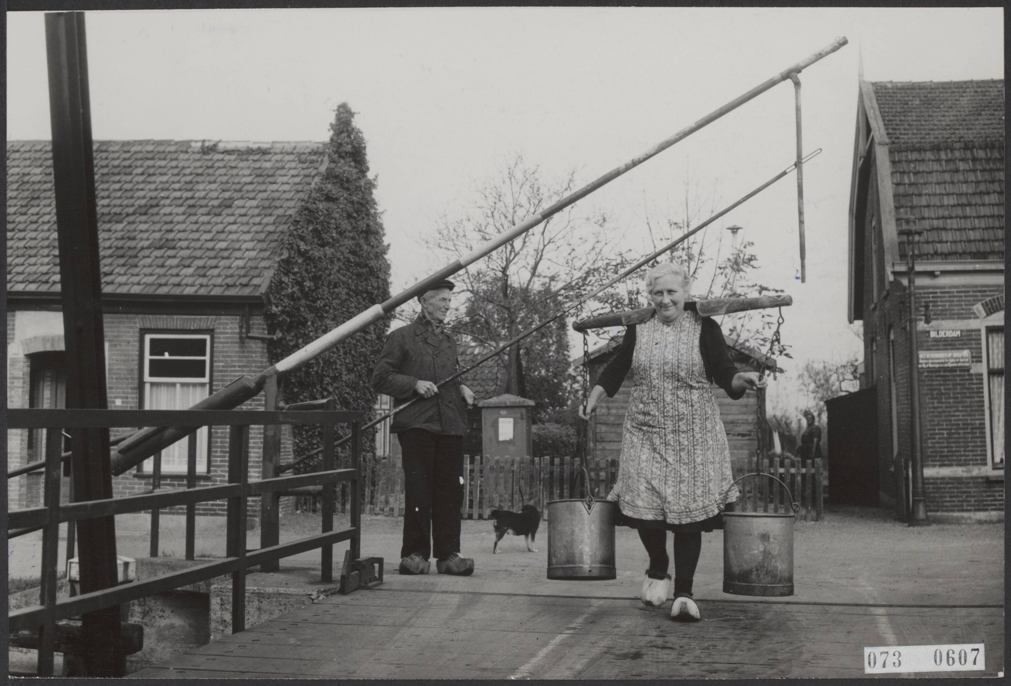 Fotocollectie Elsevier Binnenland — De 50 jaar oude tol op een houten ophaalbrug aan de Bilderdam met tolhouder B. Penning wordt nog niet opgeheven. Tolhouder Penning laat een boerin met juk met melkemmers door — Foto: Fotograaf Onbekend / Anefo. Licentie: Set B: Rechtenvrij / Publiek Domein. Bron: Nationaal Archief. http://hdl.handle.net/10648/ae151b14-d0b4-102d-bcf8-003048976d84