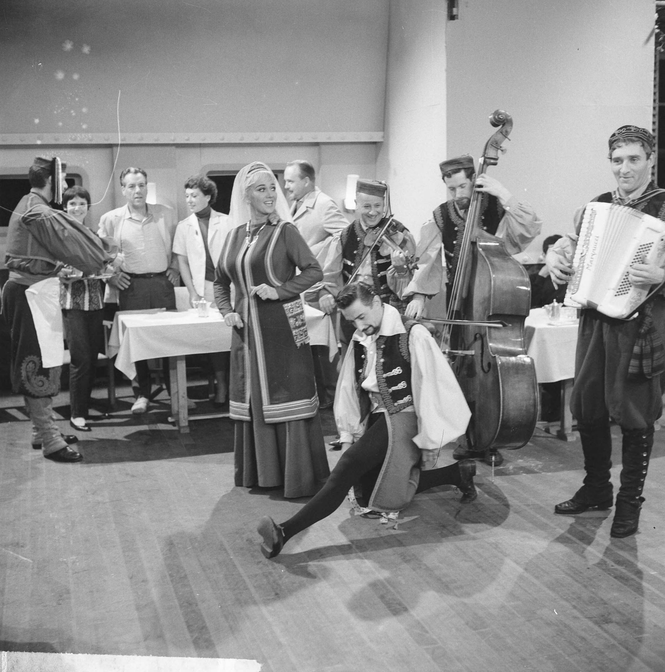 Fotocollectie Anefo — Opname televisiespel "Met 24 pk door Europa" (uitzending niet doorgegaan). De Spaanse Nederlander Marino en zijn danspartner Antonia, met begeleiders. In de achtergrond vlnr. Simone Rooskens, Ko van Dijk, Teddy Schaank en Guus Verstraete jr.Negatieven zijn een jaar later, op 31-3-1964, geregistreerd in fotoadministratie Anefo! Deze aflevering is wél uitgezonden, als eerste op 20-10-1963. Op 22-11-1963 schrijft Trouw: Er komen geen afleveringen meer van de televisiestrip "Met 24 P.K. door Europa" met Ko van Dijk, Teddy Schaank en Simone Rooskens. De AVRO heeft besloten de serie te staken. Reden: de strip kon ook na bewerking van het oorspronkelijke script niet aan de gestelde eisen voldoen. Karel Prior, hoofd amusementsprogramma's van de AVRO zei van deze door het echtpaar Mazure geschreven strip, dat ze „te filmisch" waren geschreven, waardoor men er in de televisiestudio's niet goed mee uit de voeten kon. Ellen en Georges Mazure, die zes afleveringen van hun stri