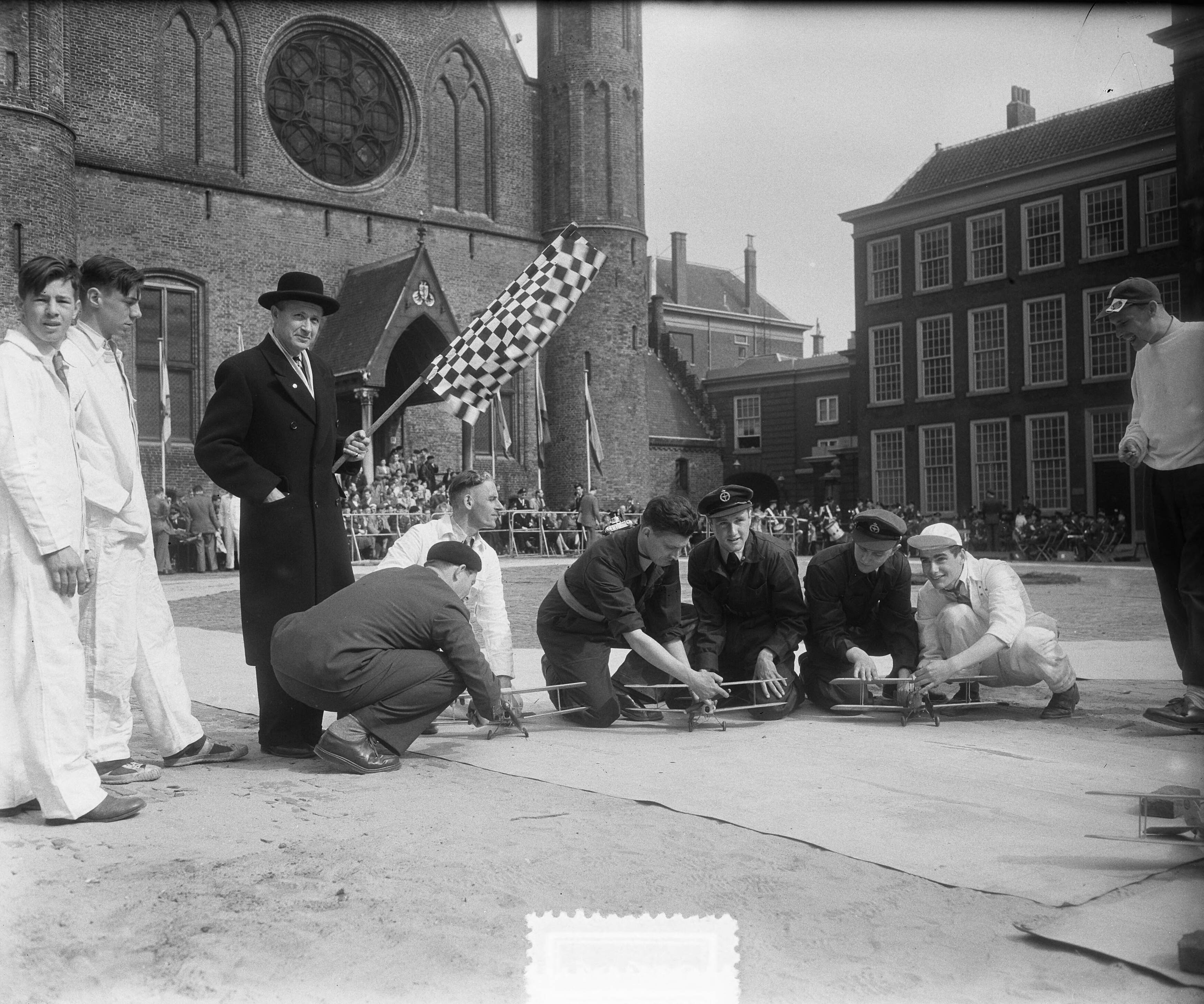 Fotocollectie Anefo — Demonstratie modelvliegtuigen op het Binnenhof te Den Haag. Directeu-generaal van de RLD Backer met de startvlag — Foto: Pot, Harry / Anefo. Licentie: Set B: Rechtenvrij / Publiek Domein. Bron: Nationaal Archief. http://hdl.handle.net/10648/a90a12fa-d0b4-102d-bcf8-003048976d84