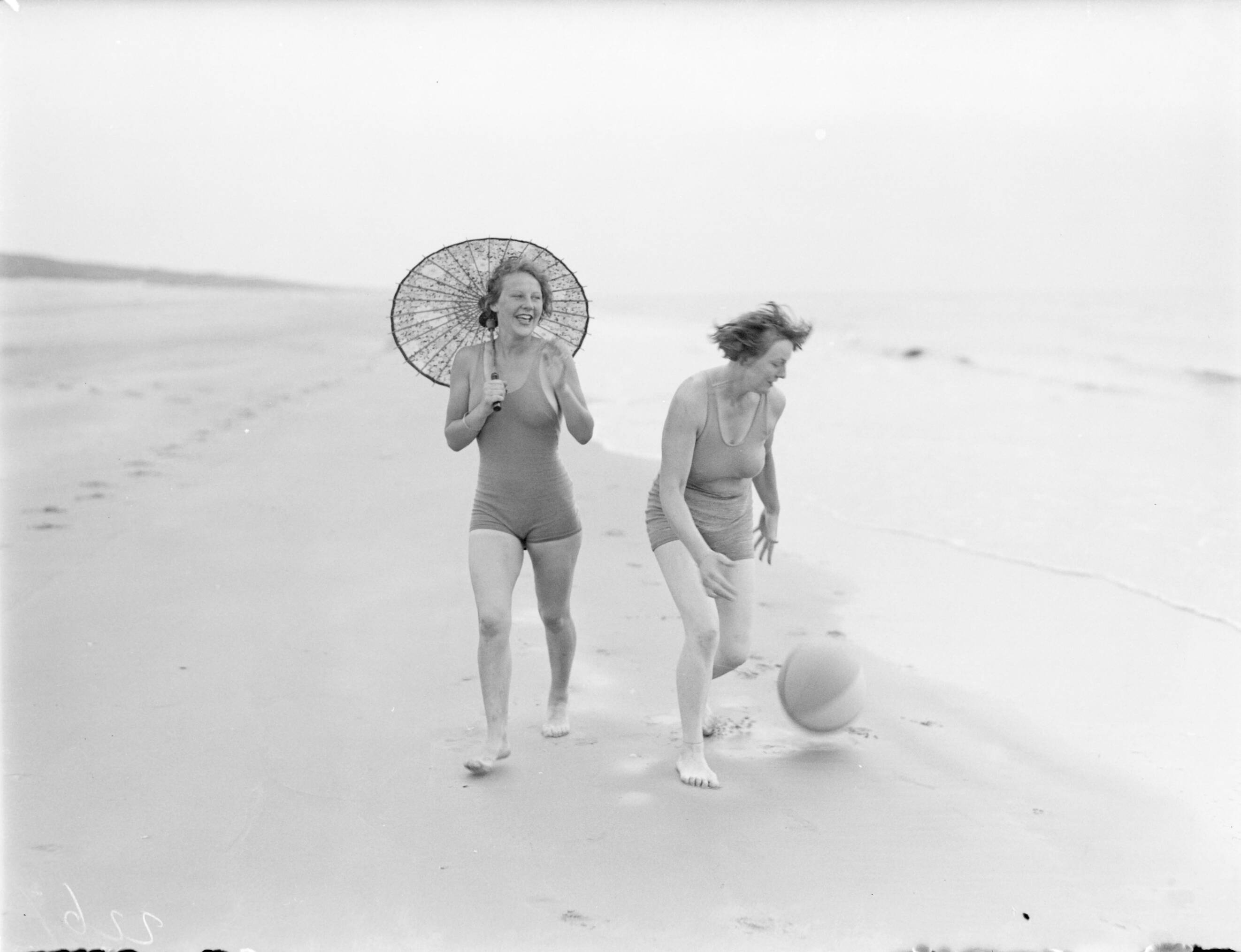Reportage fotomodel — Model Eva Waldschmidt (met parasol) en Van de Polls vrouw Nell Langlais lopen langs de vloedlijn in Zandvoort — Foto: Poll, Willem van de. Licentie: Set B: Rechtenvrij / Publiek Domein. Bron: Nationaal Archief. http://hdl.handle.net/10648/aea800c8-d0b4-102d-bcf8-003048976d84