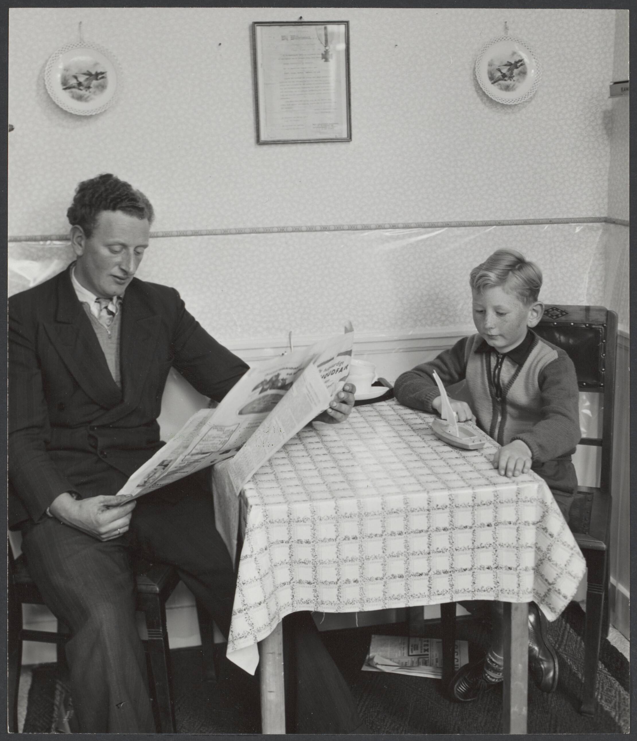Engelandvaarders / Englandspiel — Scheveningse visser Krijn Kleijn, die in 1941, met nog 6 anderen, in 'n vlot naar Engeland was overgestoken en door koningin Wilhelmina werd ontvangen [aan tafel met een zoon? Aan de muur hangt oorkonde van koningin Wilhelmina met onderscheiding] — Foto: Stuifbergen, Wilh. L. (Pim) / Spaarnestad (1). Licentie: Set B: Rechtenvrij / Publiek Domein. Bron: Nationaal Archief. http://hdl.handle.net/10648/5082c233-544e-6ae4-f239-ff23e7977eff