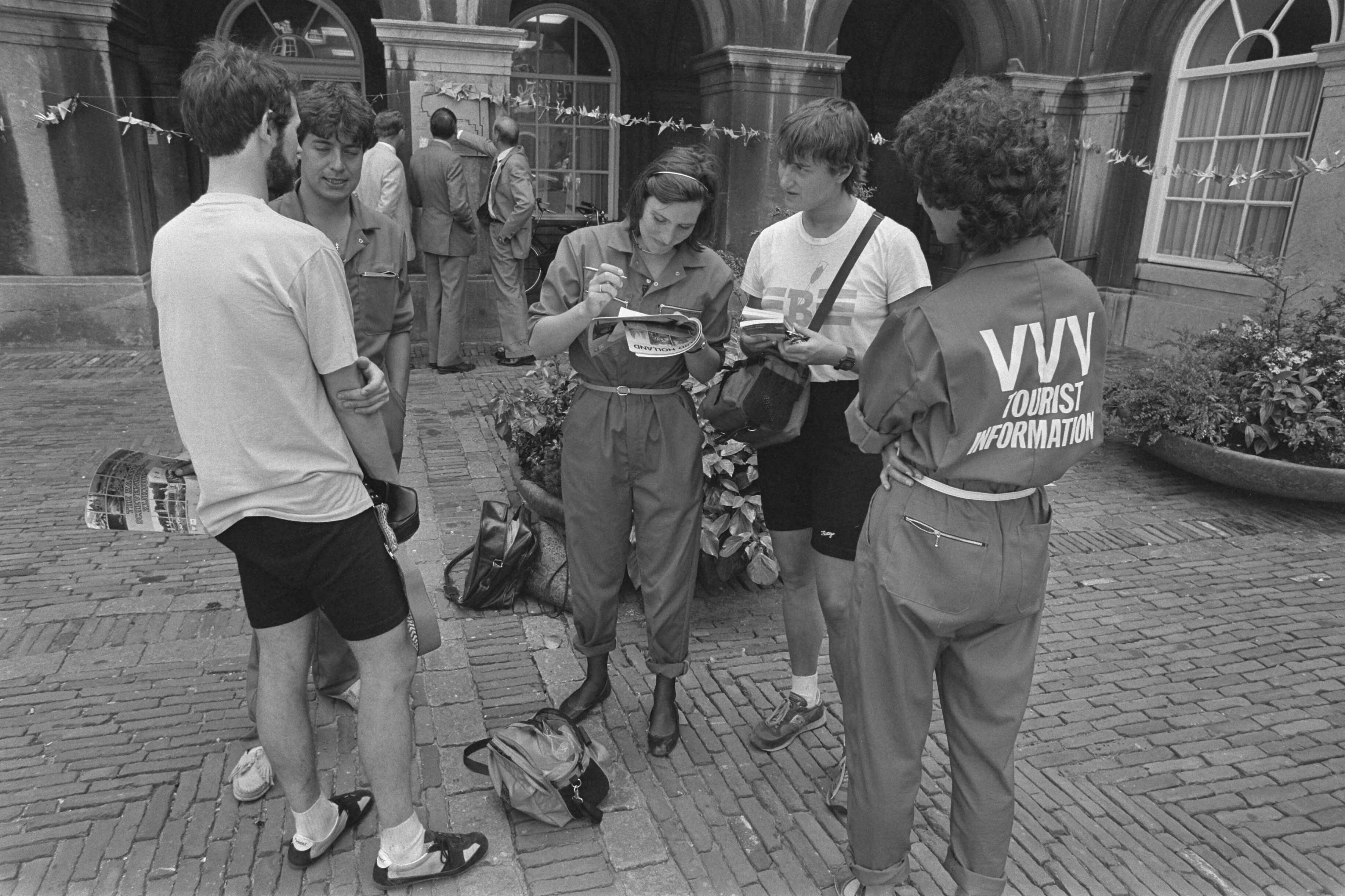 Fotocollectie Anefo — Werklozen "werken" voor de VVV in Den Haag ; enkele in "VVV-overall" gestoken werklozen helpen touristen op het Binnenhof — Foto: Bogaerts, Rob / Anefo. Licentie: Set B: Rechtenvrij / Publiek Domein. Bron: Nationaal Archief. http://hdl.handle.net/10648/ad3a455c-d0b4-102d-bcf8-003048976d84