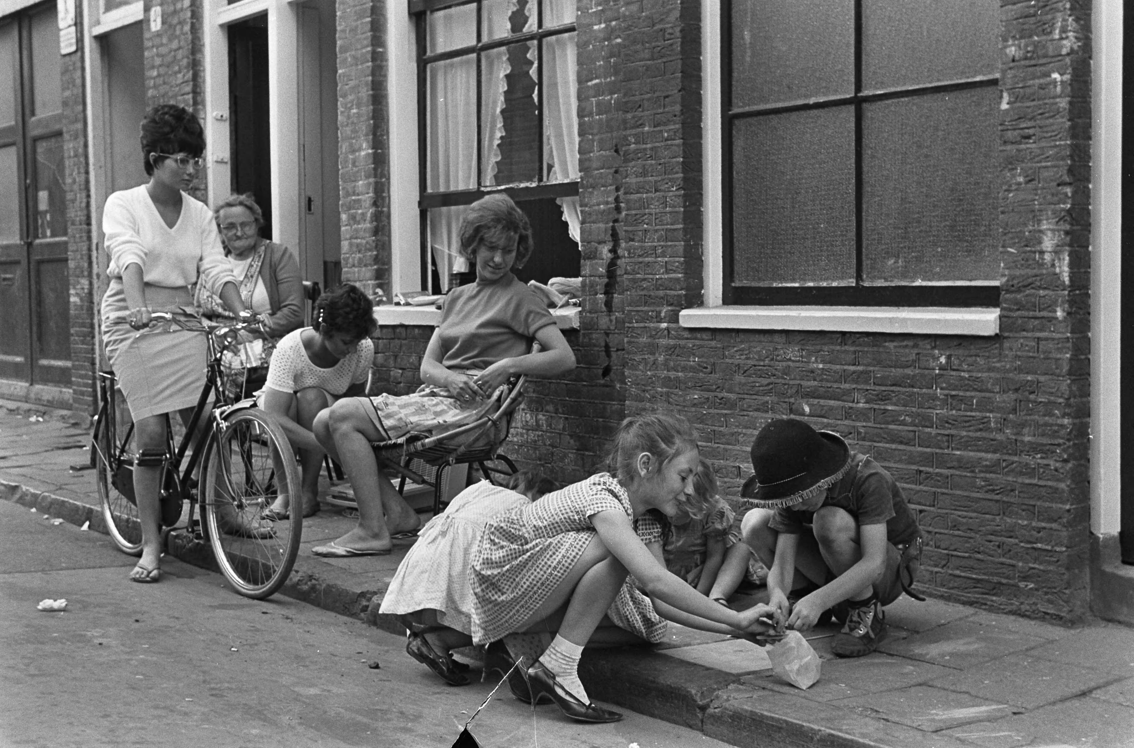 Fotocollectie Anefo — Zomer in de Jordaan (Amsterdam), moeders zitten buiten met spelende kinderen op straat — Foto: Evers, Joost / Anefo. Licentie: Set B: Rechtenvrij / Publiek Domein. Bron: Nationaal Archief. http://hdl.handle.net/10648/aabba87a-d0b4-102d-bcf8-003048976d84