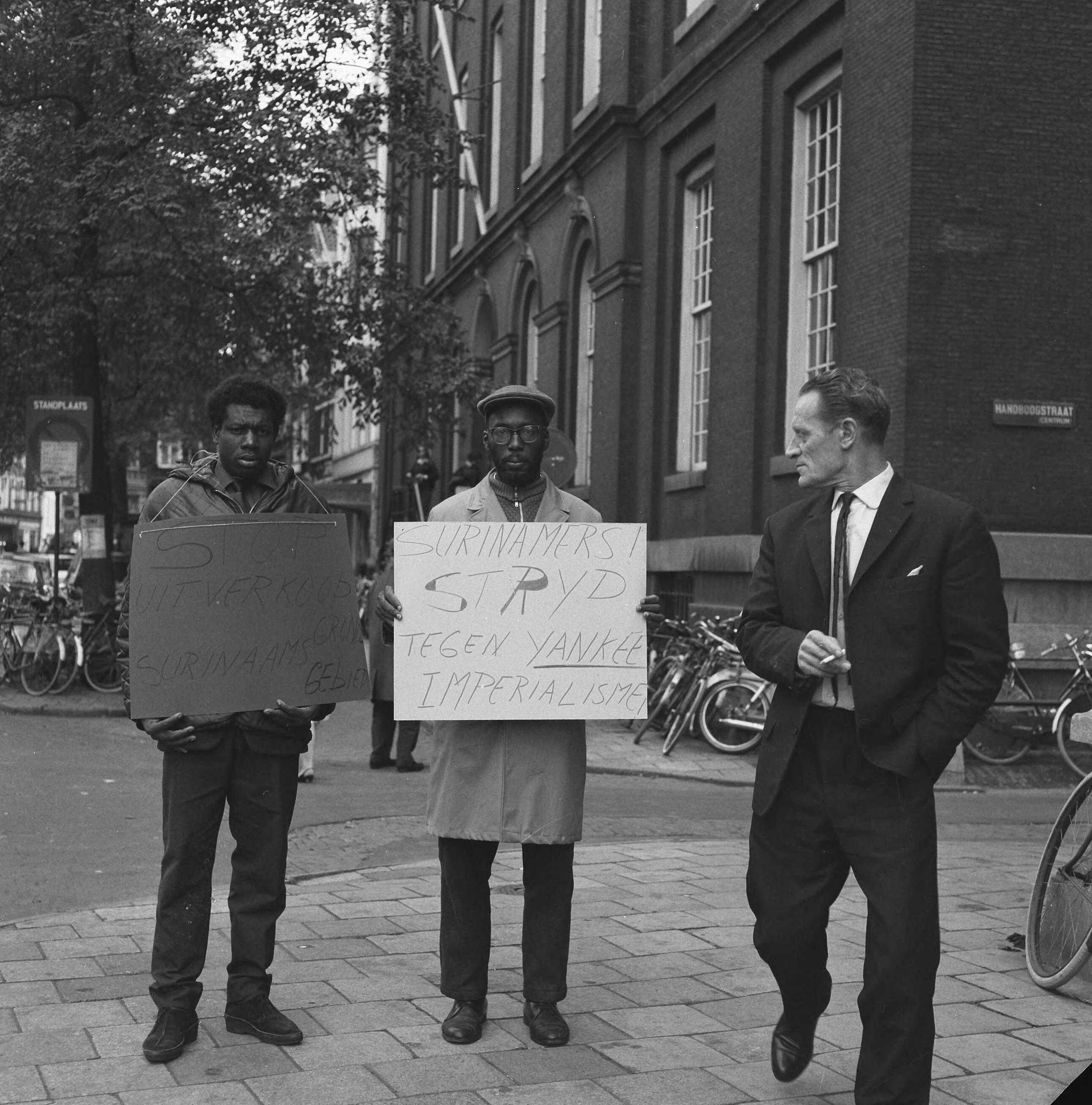 Fotocollectie Anefo — Surinaamse studenten voor het Maagdenhuis in Amsterdam, protesterend tegen het bezoek van koningin Juliana aan Suriname — Foto: Kroon, Ron / Anefo. Licentie: Set B: Rechtenvrij / Publiek Domein. Bron: Nationaal Archief. http://hdl.handle.net/10648/aac4b3b6-d0b4-102d-bcf8-003048976d84