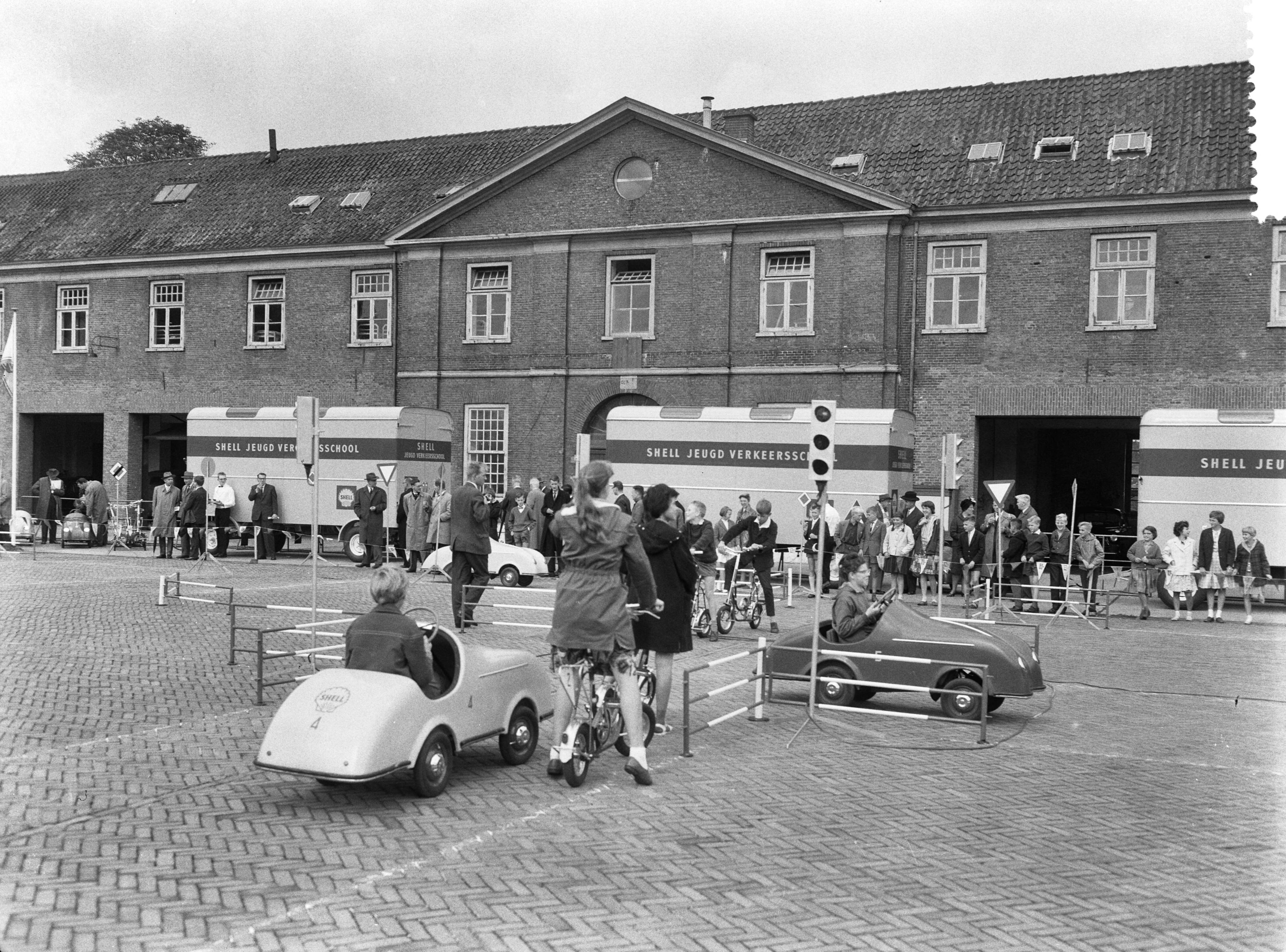 Fotocollectie Anefo — Overhandiging Mobiele Verkeersscholen door de Shell aan het Verbond voor Veilig Verkeer in Den Haag. De verkeersplaats met trapauto's en fietsen. In de achtergrond de trailers met opschrift "Shell Jeugd Verkeersschool" waarin de verkeerschoolattributen vervoerd kunnen worden — Foto: Thuring, John / Anefo. Licentie: Set B: Rechtenvrij / Publiek Domein. Bron: Nationaal Archief. http://hdl.handle.net/10648/a9e17e98-d0b4-102d-bcf8-003048976d84