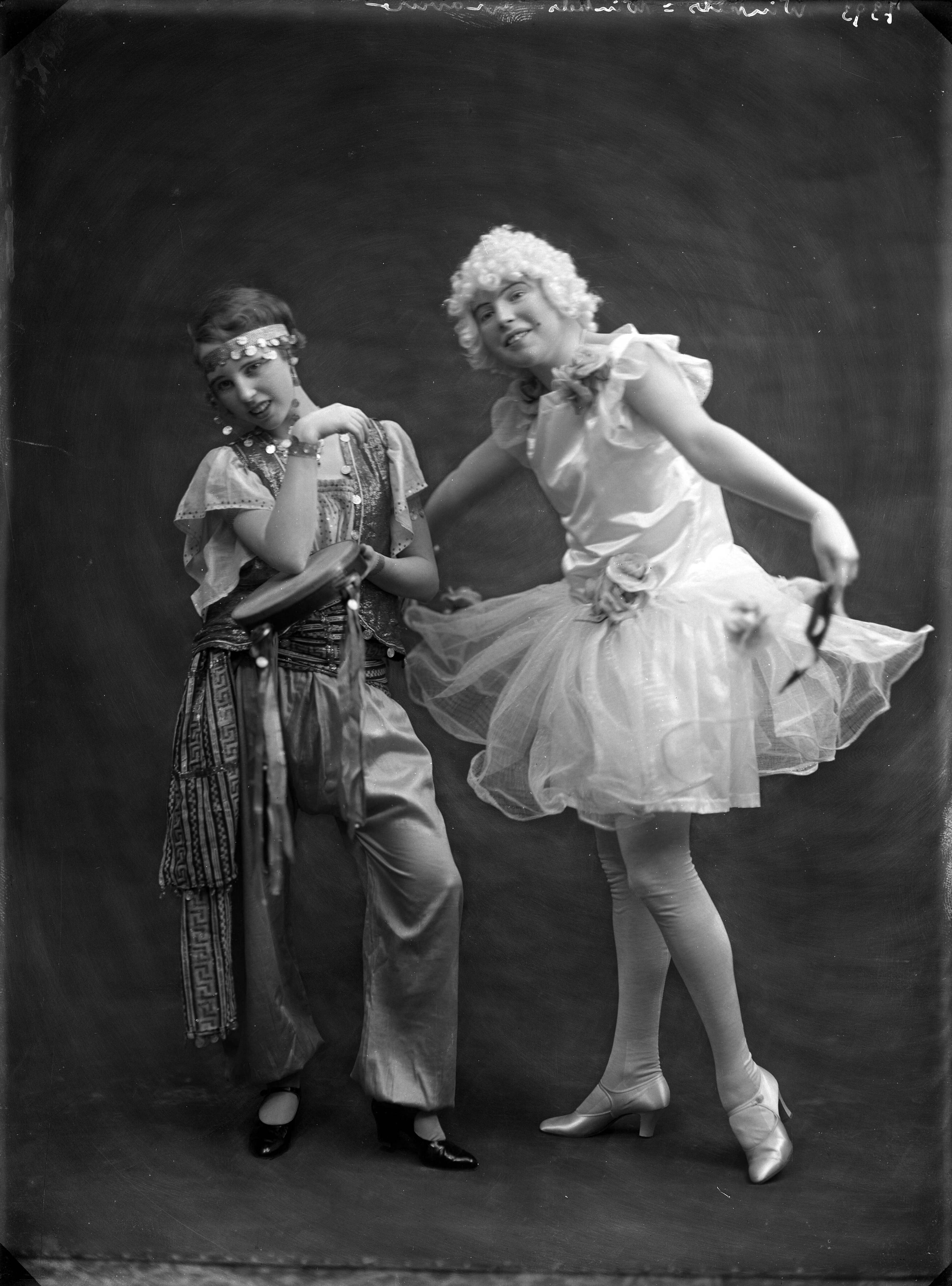 Economie, handel, industrie, bouw, arbeid — Studio-opname van twee jonge meisjes in carnavalskleding. Een meisje in een Mata Hari-achtige outfit, het andere meisje in een witte ballerinajurkje met wijde organzarok. 7393 Winkels = Winkels gravure. Haarlem, Nederland. 1918-1930 — Foto: Berg, Th.C.J. van den / Spaarnestad Photo (05887). Licentie: Set B: Rechtenvrij / Publiek Domein. Bron: Nationaal Archief. http://hdl.handle.net/10648/35429da7-c54f-a382-e063-6df0900a6686