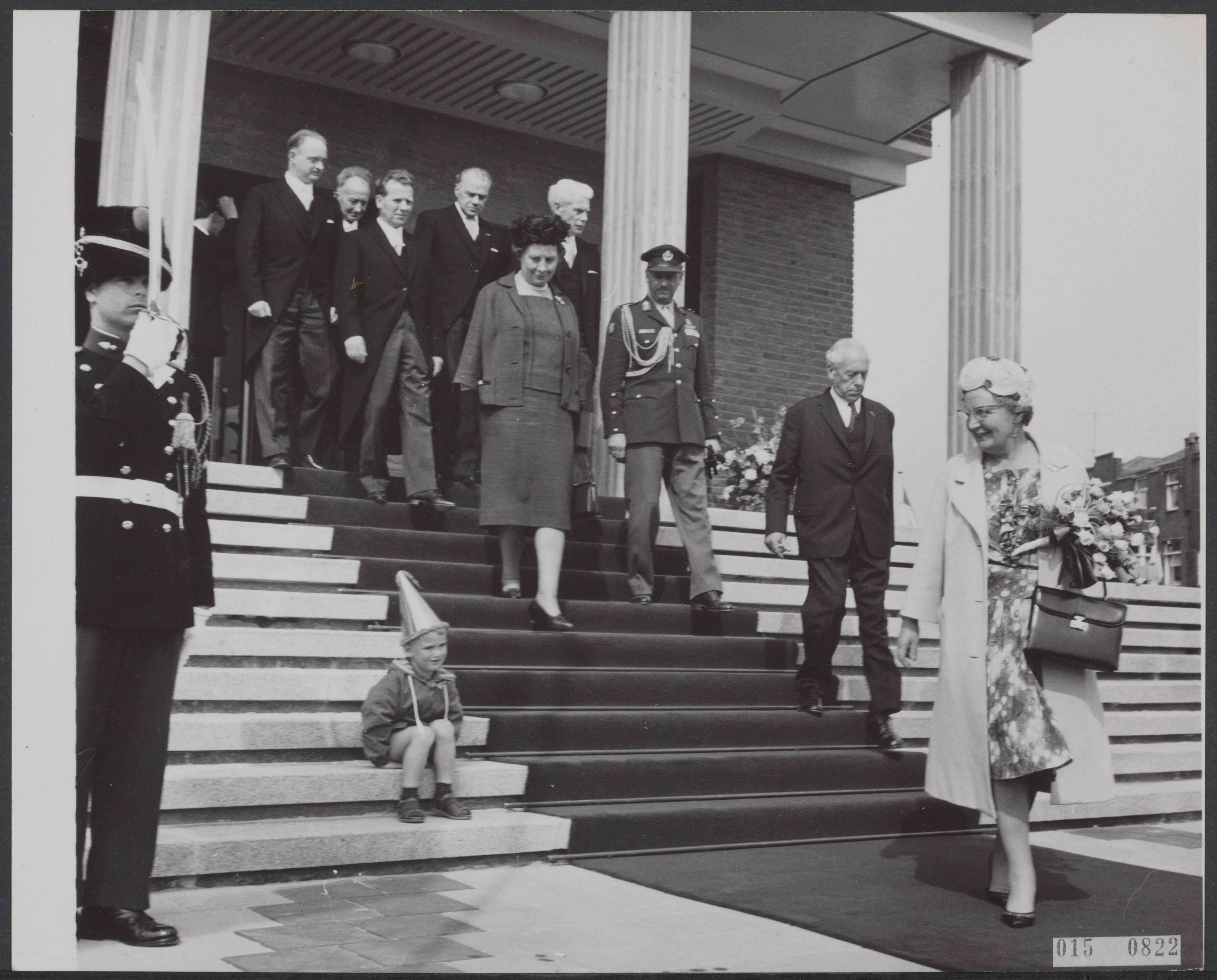Fotocollectie Elsevier Binnenland — Koningin Juliana kijkt bij het verlaten van het nieuwe stadhuis van Vlissingen, naar een kleine jongen met feestmuts die plaatsgenomen heeft op de trappen van het nieuwe stadhuis — Foto: Nijs, Jac. de / Anefo. Licentie: Set B: Rechtenvrij / Publiek Domein. Bron: Nationaal Archief. http://hdl.handle.net/10648/adb6438c-d0b4-102d-bcf8-003048976d84