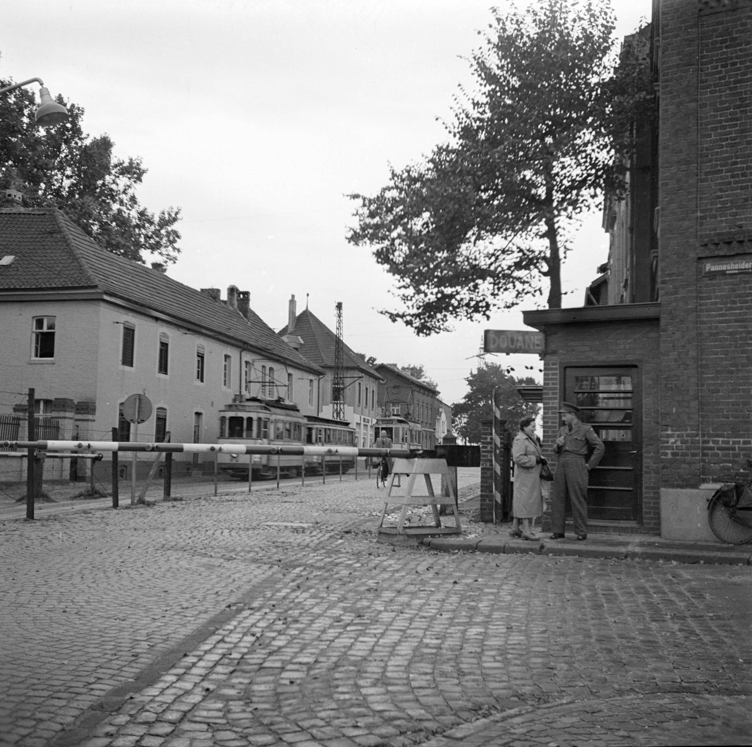 Zuid-Limburg — Hildegard Eschen in gesprek met een douanebeambte bij de grensovergang in de Nieuwstraat — Foto: Poll, Willem van de. Licentie: Set B: Rechtenvrij / Publiek Domein. Bron: Nationaal Archief. http://hdl.handle.net/10648/aea62640-d0b4-102d-bcf8-003048976d84