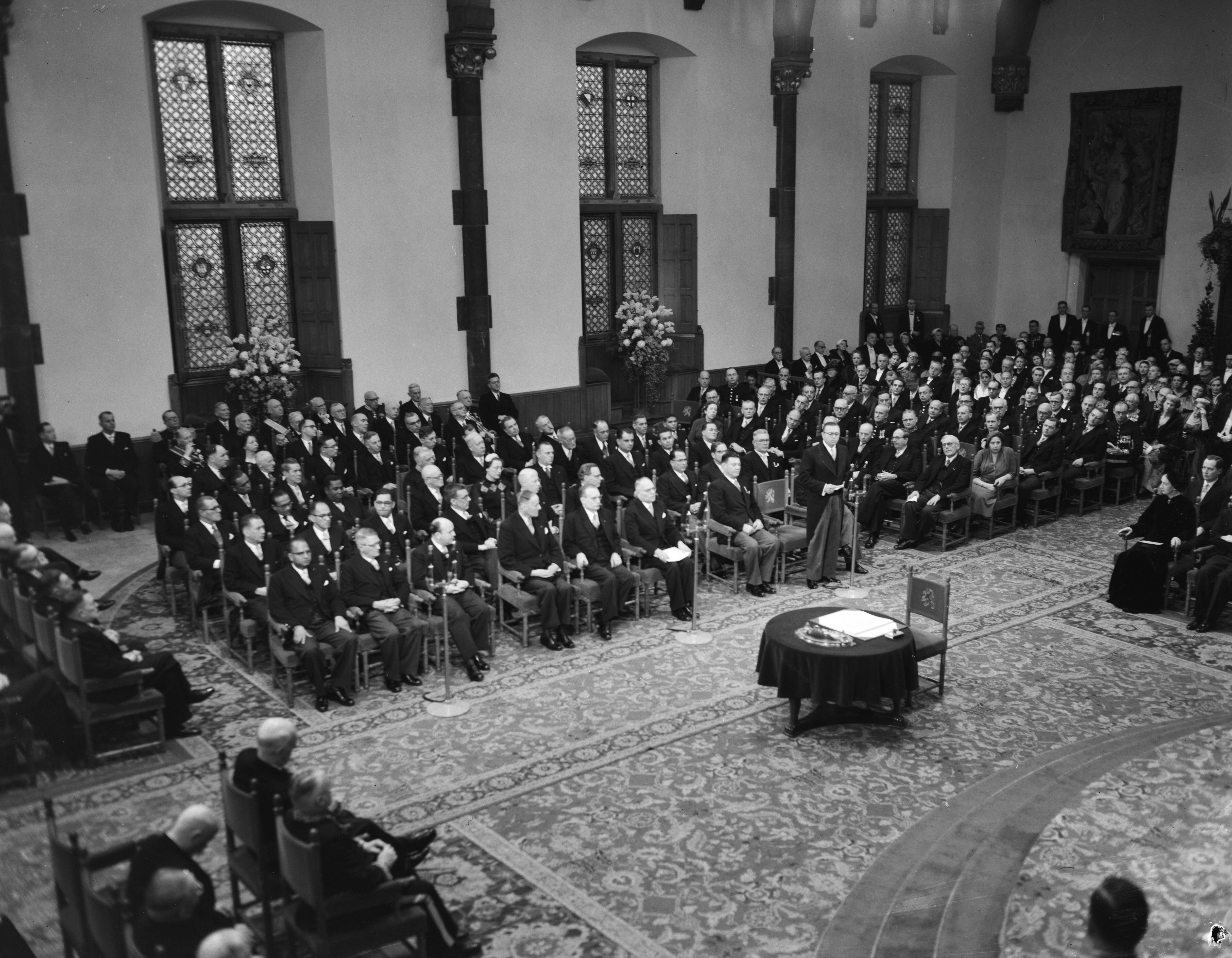 Koningin Juliana ondertekent in een plechtige bijeenkomst in de Ridderzaal in Den Haag de Acte van Bevestiging van het Statuut voor het Koninkrijk — Ondertekening van de Acte van Bevestiging van het Statuut van het Koninkrijk in de Ridderzaal te Den Haag. Één van de ministers houdt een toespraak — Foto: Noske, J.D. / Anefo. Licentie: Set B: Rechtenvrij / Publiek Domein. Bron: Nationaal Archief. http://hdl.handle.net/10648/a92e1a42-d0b4-102d-bcf8-003048976d84