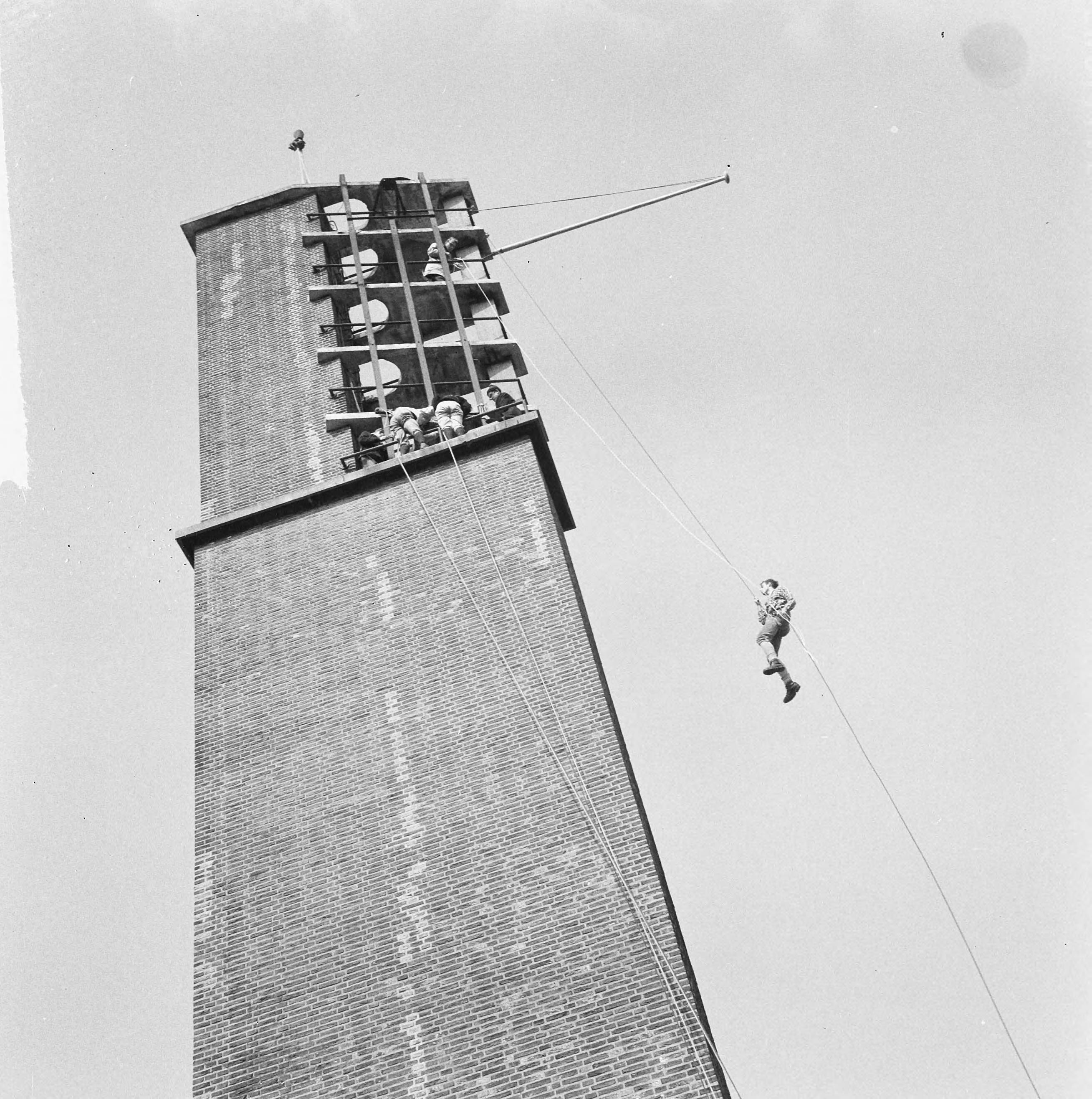 Fotocollectie Anefo — Kamp Houtrust 1965 geopend door wethouder mr. M. Vrolijk van Den Haag, leden van de Delftse Studenten Alpenclub tijdens het "abseilen" van de 32 meter hoge toren van de Houtrusthallen — Foto: Nijs, Jac. de / Anefo. Licentie: Set B: Rechtenvrij / Publiek Domein. Bron: Nationaal Archief. http://hdl.handle.net/10648/aa9ee71c-d0b4-102d-bcf8-003048976d84
