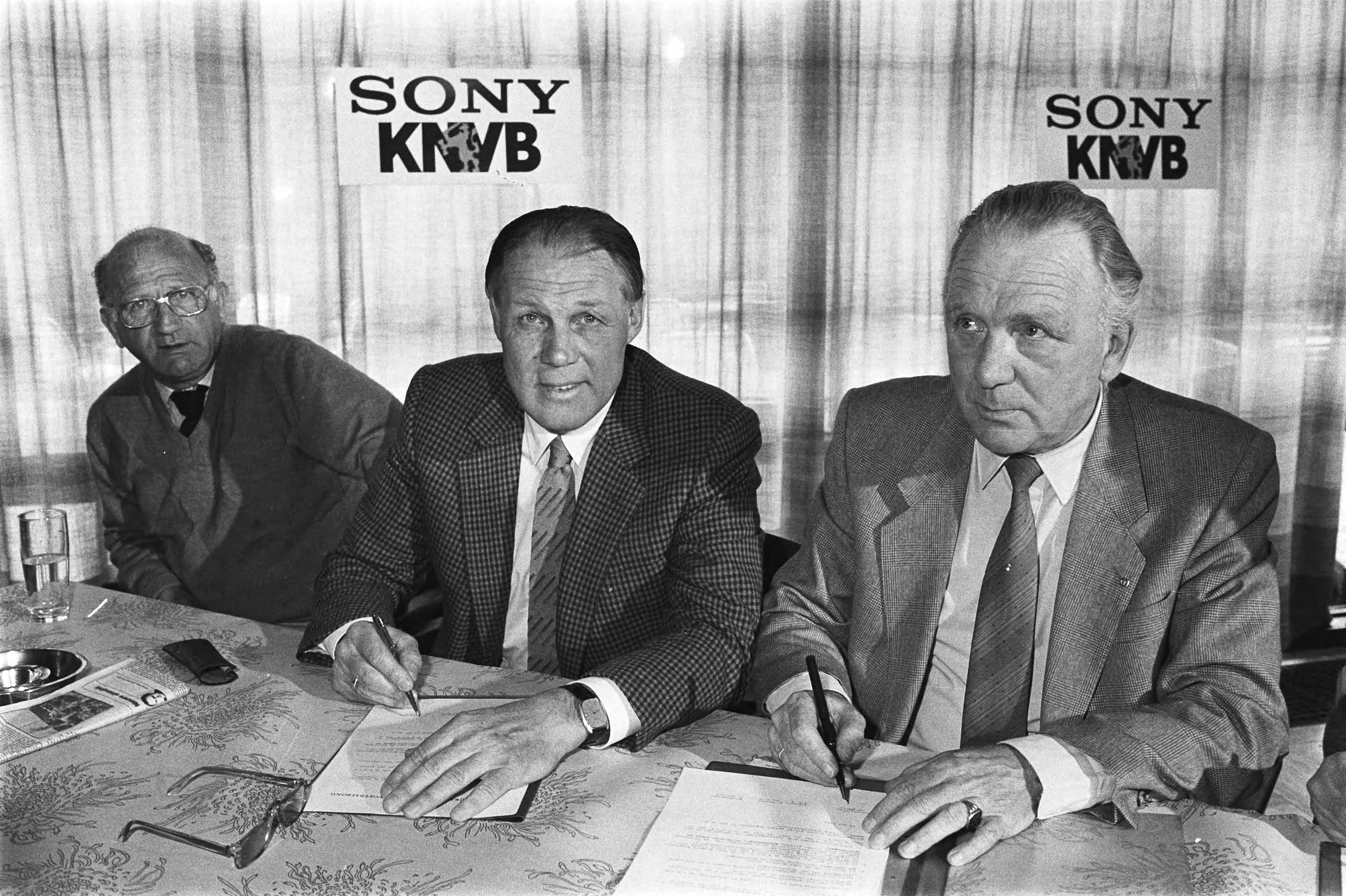 Fotocollectie Anefo — Zeist, Rinus Michels tekent contract voor technisch coordinator bij de KNVB; Rinus Michels tekent contract, links bondscoach Rijvers, rechts KNVB-voorz. — Foto: Antonisse, Marcel / Anefo. Licentie: Set B: Rechtenvrij / Publiek Domein. Bron: Nationaal Archief. http://hdl.handle.net/10648/ad38b58e-d0b4-102d-bcf8-003048976d84