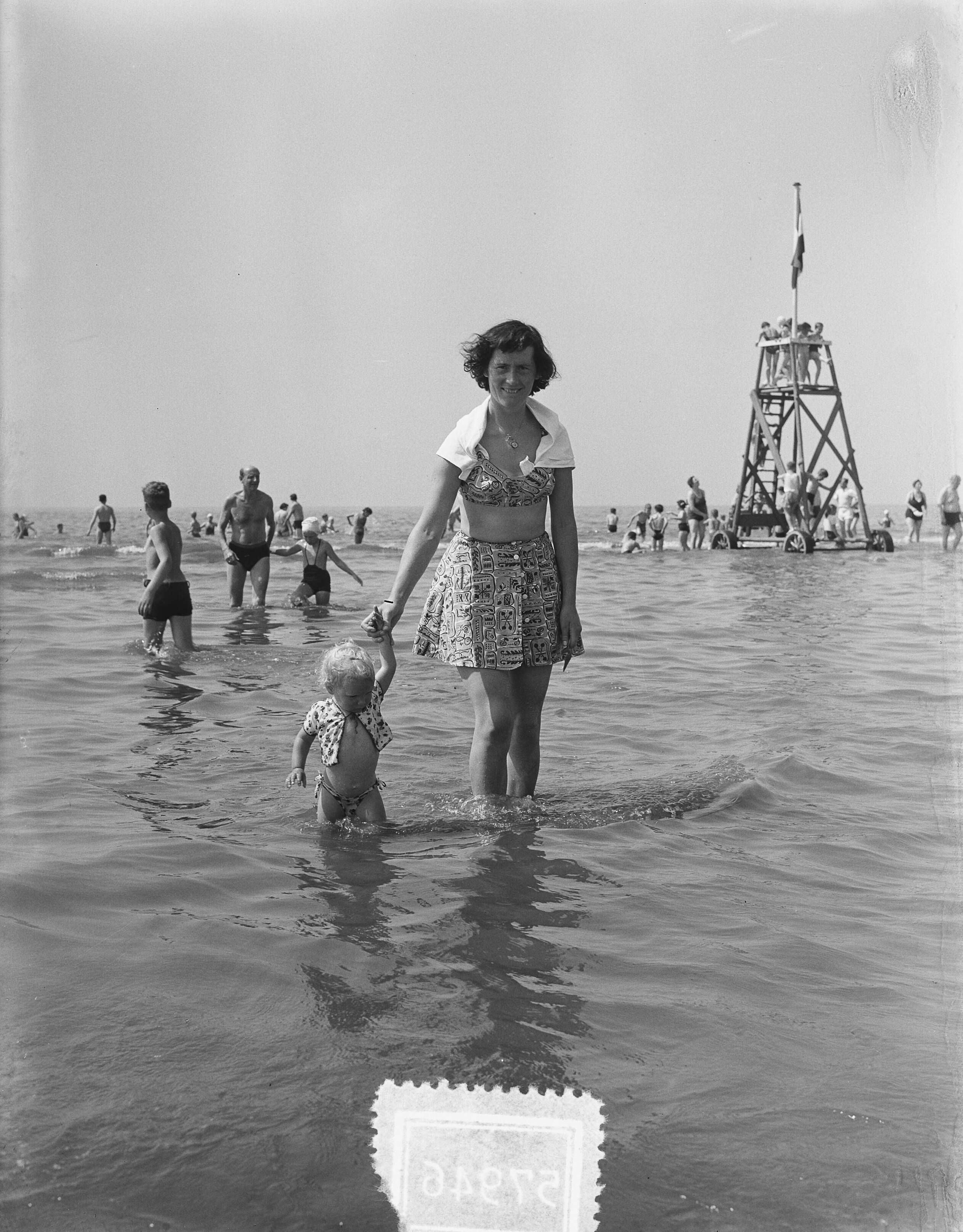 Fotocollectie Anefo — Zomerplaatjes. Drukte op het strand van Zandvoort. Vrouw met kind in het water — Foto: Rossem, Wim van / Anefo. Licentie: Set B: Rechtenvrij / Publiek Domein. Bron: Nationaal Archief. http://hdl.handle.net/10648/a90e3614-d0b4-102d-bcf8-003048976d84
