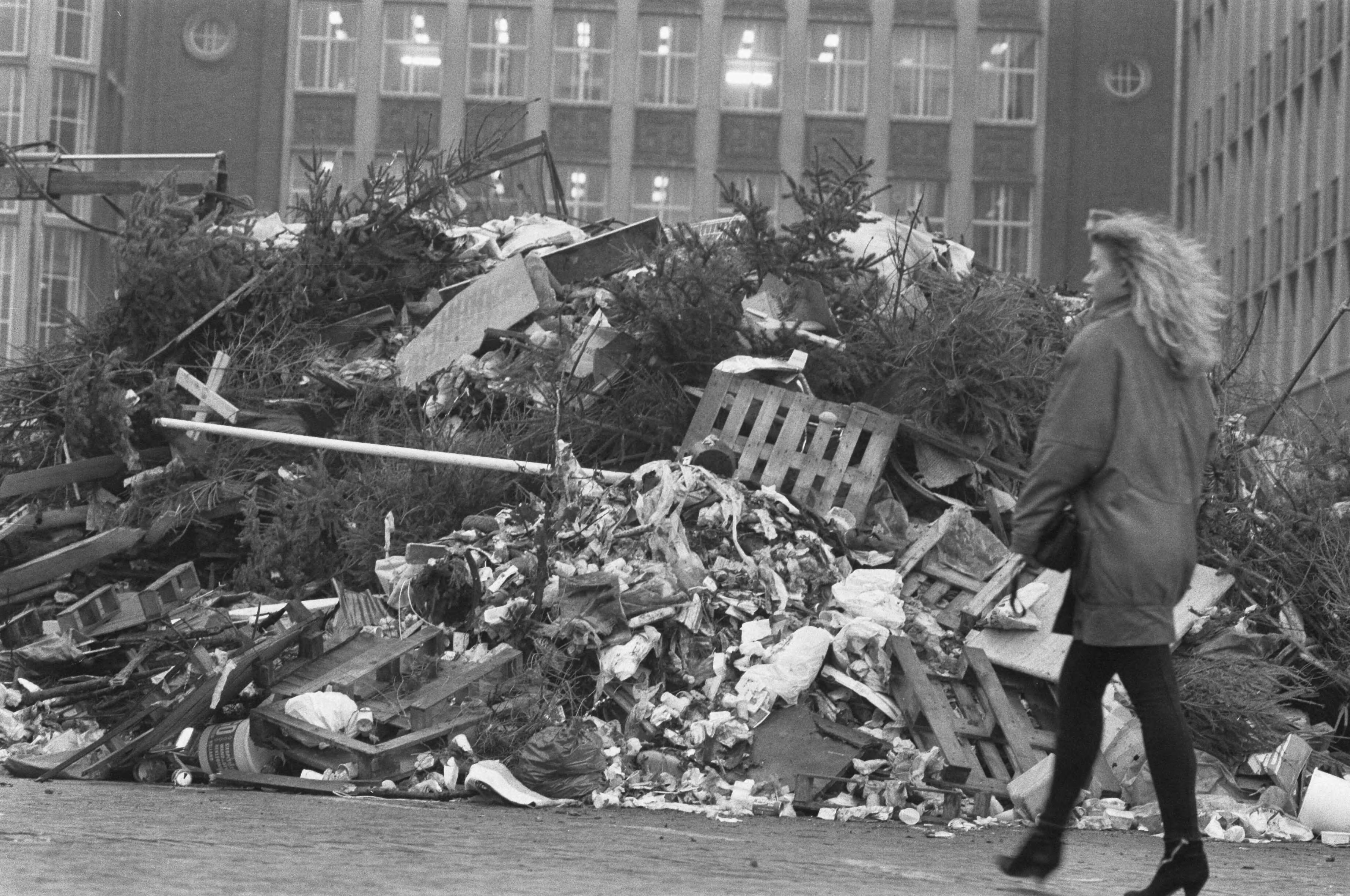 Plantsoenendienst Den Haag gooit vuil voor het stadhuis voor vuilwerktoeslag — Een vrouw loopt voorbij de berg vuil — Foto: Bogaerts, Rob / Anefo. Licentie: Set B: Rechtenvrij / Publiek Domein. Bron: Nationaal Archief. http://hdl.handle.net/10648/ad6f9ad6-d0b4-102d-bcf8-003048976d84