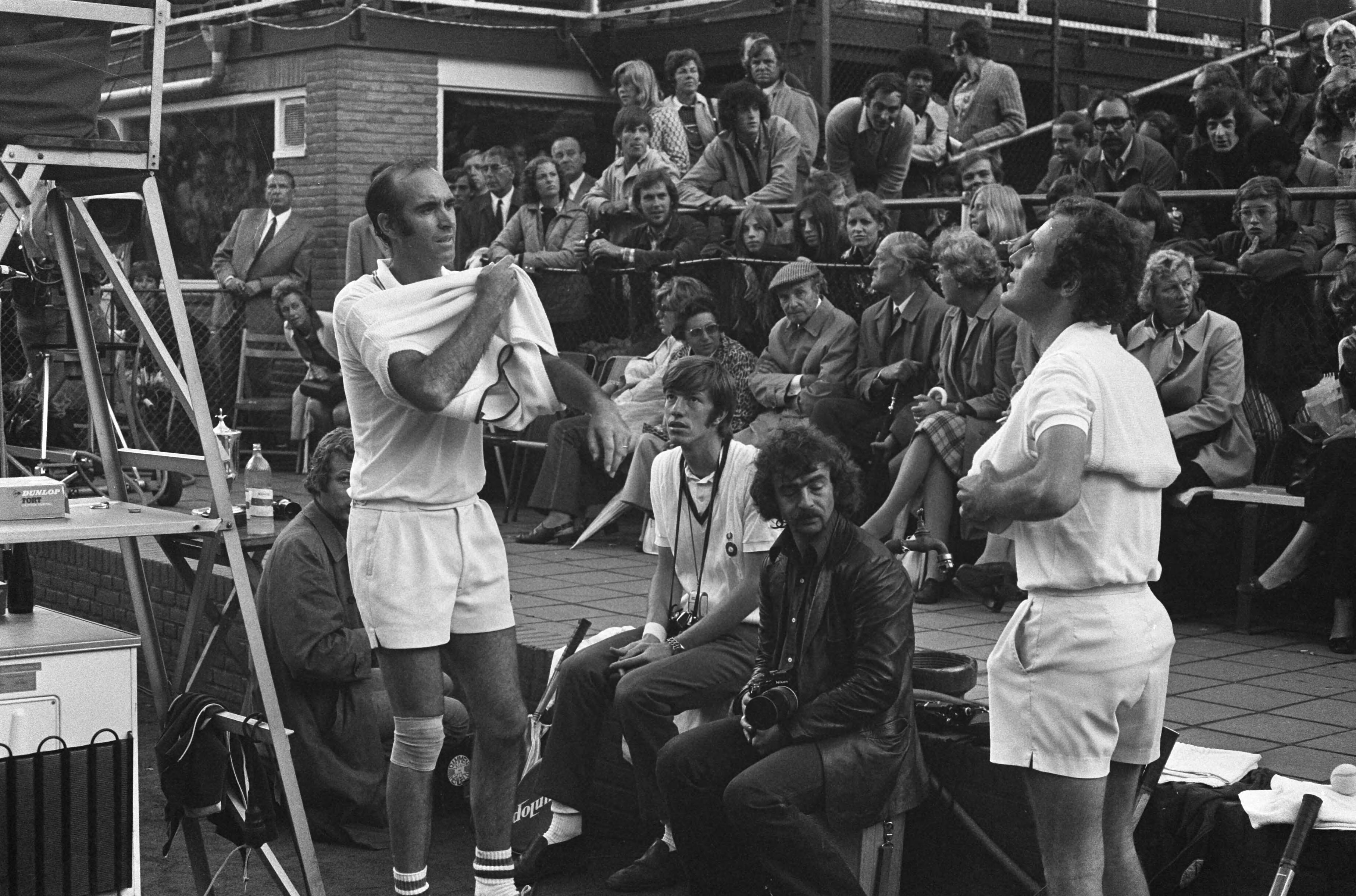 Fotocollectie Anefo — Internationale Tenniskampioenchappen Melkhuisje, nummer en 20A Tom Okker (rechts) en Gimeno rusten — Foto: Punt, W. / Anefo. Licentie: Set B: Rechtenvrij / Publiek Domein. Bron: Nationaal Archief. http://hdl.handle.net/10648/ac323dc2-d0b4-102d-bcf8-003048976d84