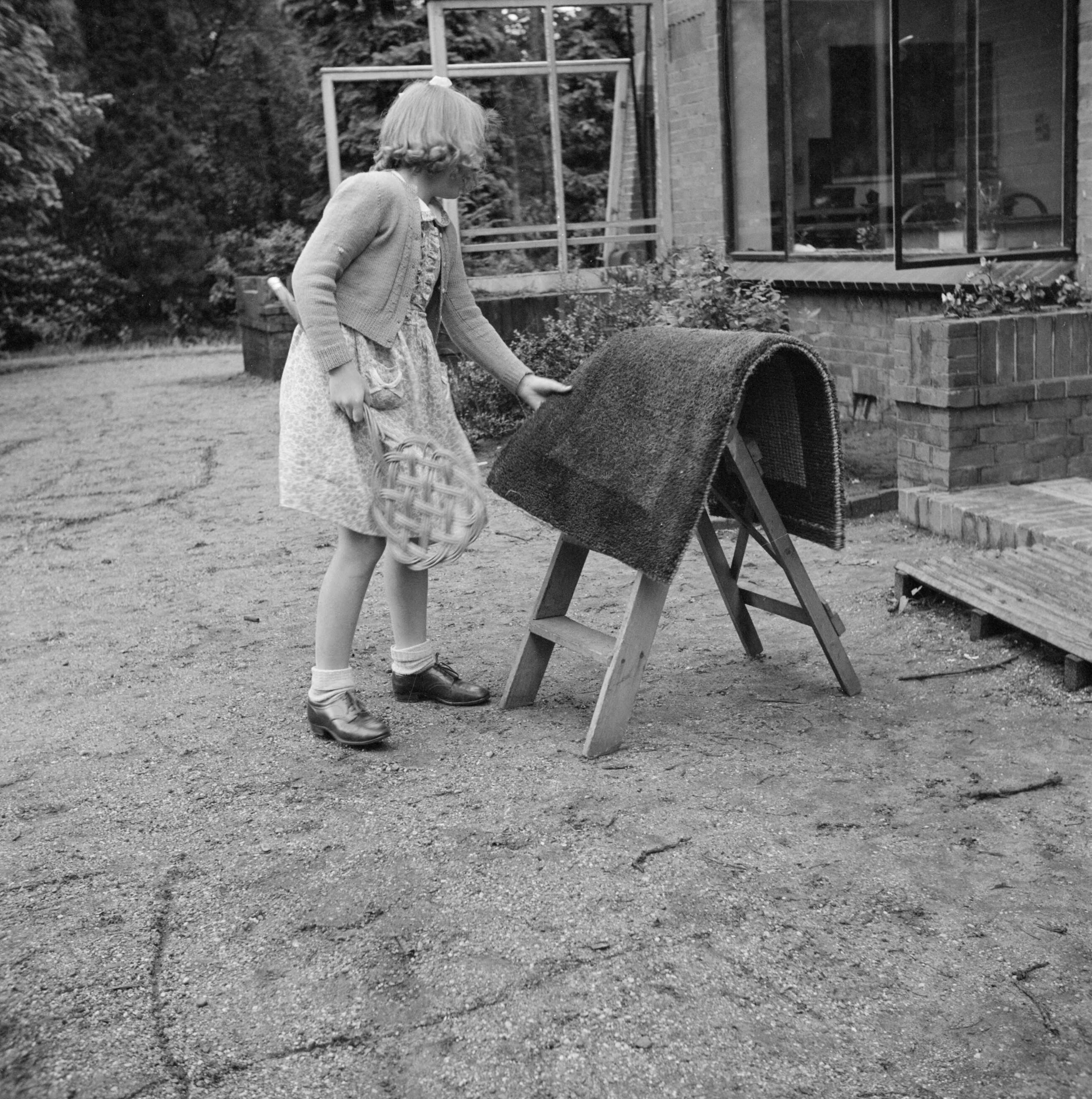 Prinses Beatrix en prinses Irene op de Werkplaats Kindergemeenschap van Kees Boeke te Bilthoven — Prinses Beatrix klopt een deurmat — Foto: Poll, Willem van de. Licentie: Set B: Rechtenvrij / Publiek Domein. Bron: Nationaal Archief. http://hdl.handle.net/10648/aee82482-d0b4-102d-bcf8-003048976d84