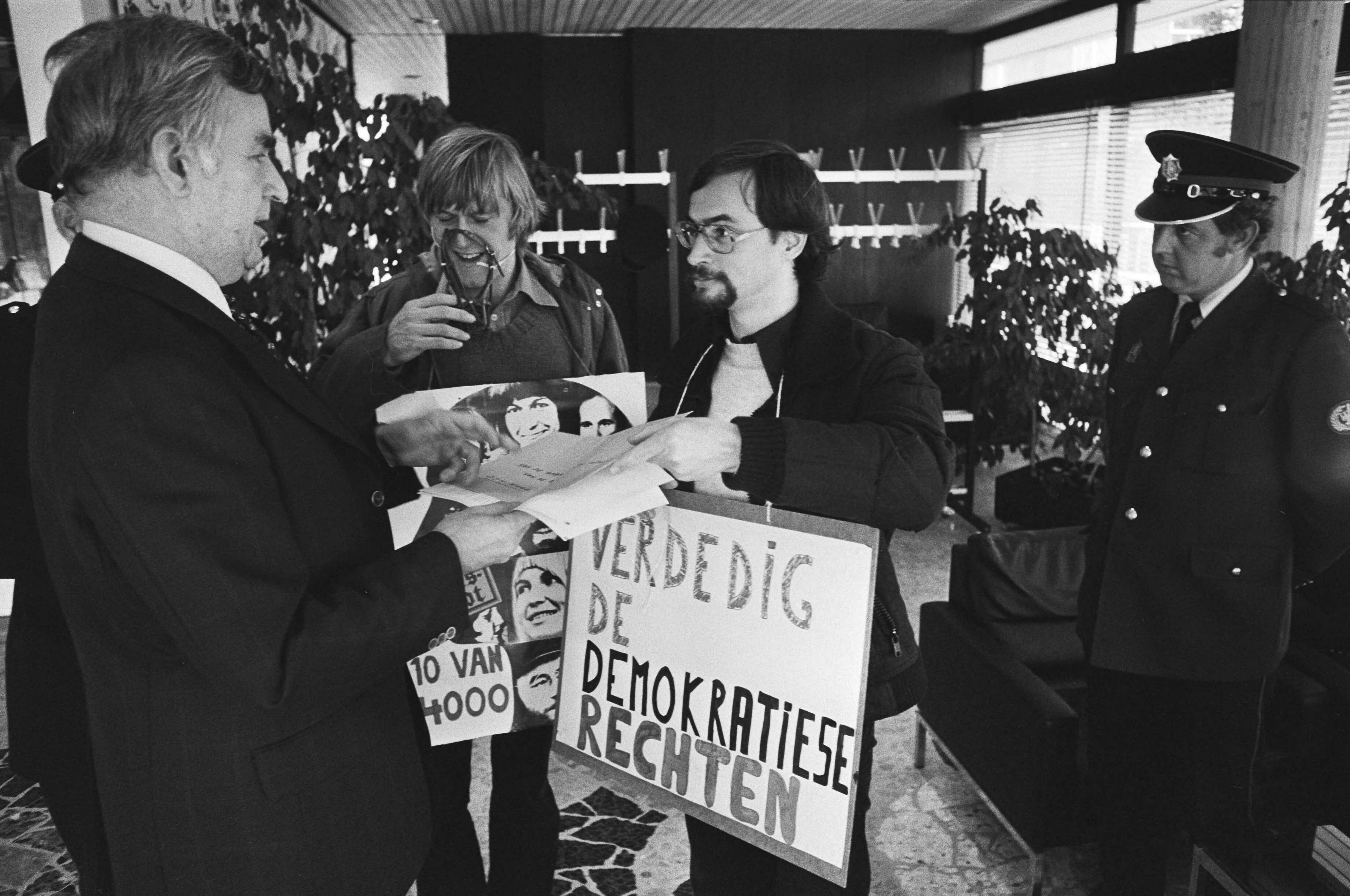 Fotocollectie Anefo — Demonstratie tegen Berufsverbott voor ambassade BRD in Den Haag , gemuilkorfde demonstranten — Foto: Verhoeff, Bert / Anefo. Licentie: Set B: Rechtenvrij / Publiek Domein. Bron: Nationaal Archief. http://hdl.handle.net/10648/acbd1ffa-d0b4-102d-bcf8-003048976d84