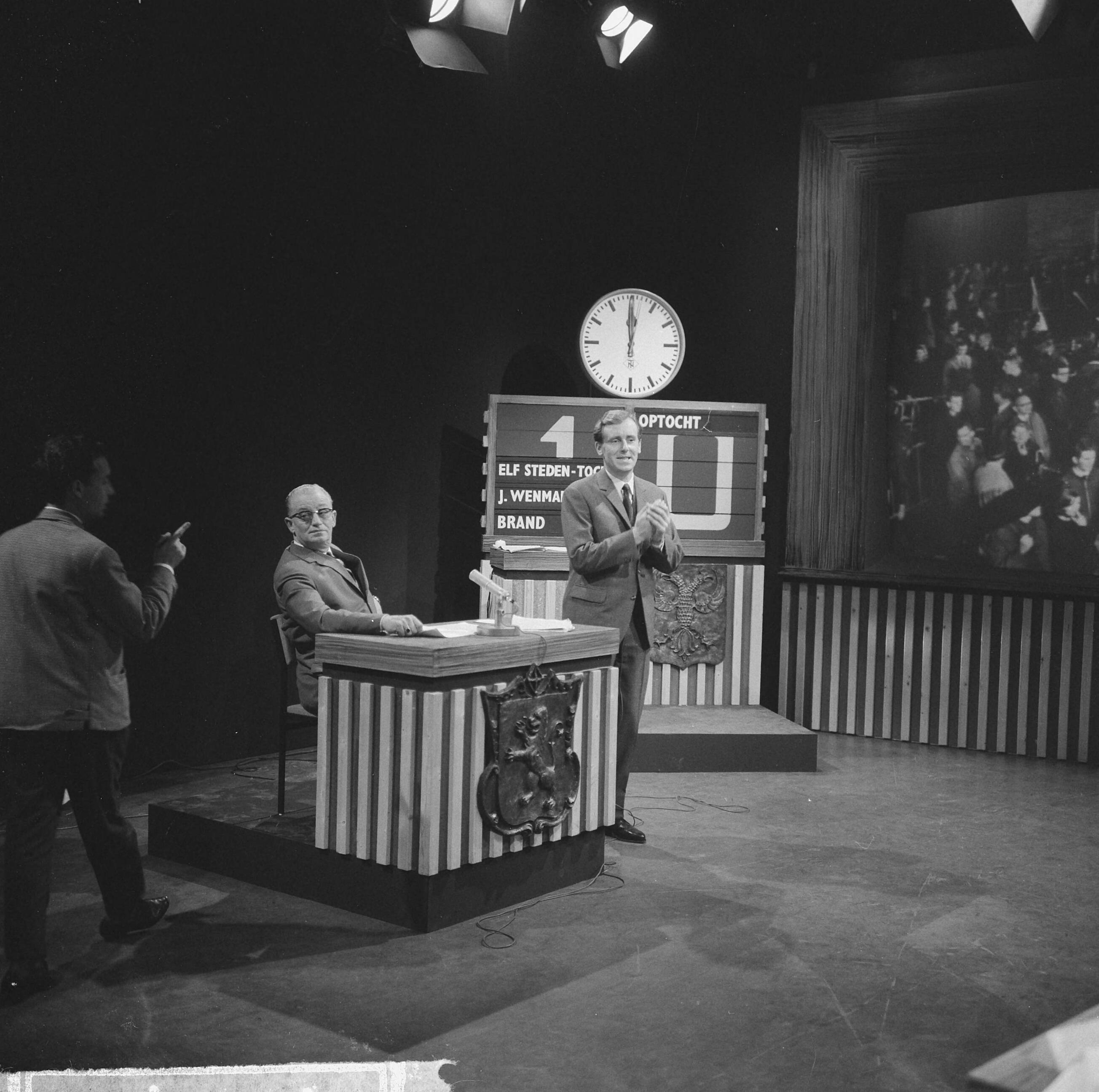 Fotocollectie Anefo — NCRV-quiz 'Een tegen allen' tussen Zierikzee en Bolsward, In de studio te Bussum, achter de desk de opdrachtengever, de heer Doeleman uit Zierikzee, daarnaast spelleider Dick van Ruler, op achtergrond televisiescherm met beelden uit Bolsward — Foto: Nijs, Jac. de / Anefo. Licentie: Set B: Rechtenvrij / Publiek Domein. Bron: Nationaal Archief. http://hdl.handle.net/10648/aa7f3714-d0b4-102d-bcf8-003048976d84