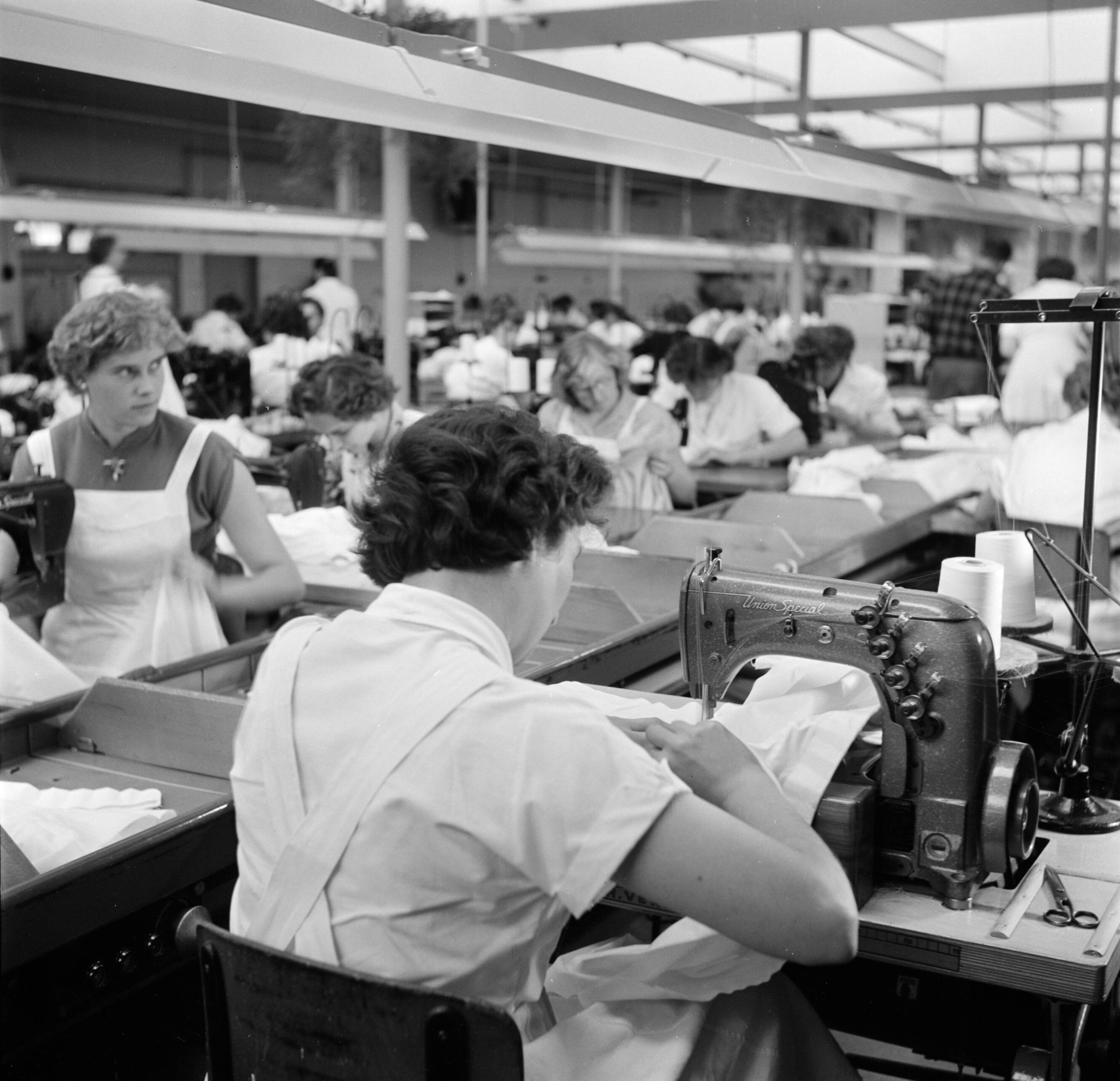 Reportage Kerko Haarlem — Zaal met naaisters aan naaimachine bij overhemdenbedrijf Kerko — Foto: Poll, Willem van de. Licentie: Set B: Rechtenvrij / Publiek Domein. Bron: Nationaal Archief. http://hdl.handle.net/10648/aecbc5f8-d0b4-102d-bcf8-003048976d84