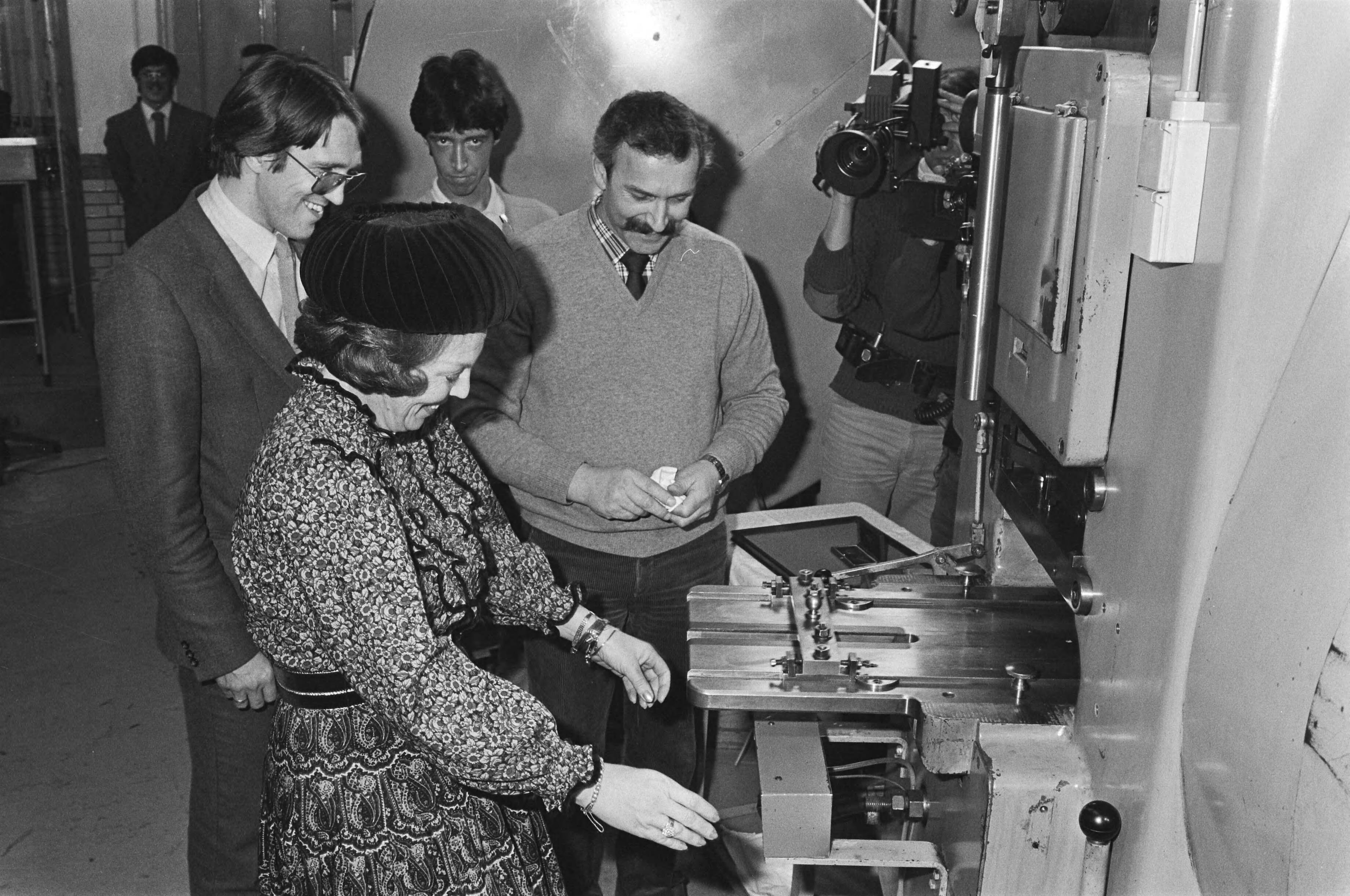 Fotocollectie Anefo — Koningin Beatrix slaat ook eerste nieuwe guldens in Rijksmunt te Utrecht. Beatrix achter machine die guldens maakt — Foto: Antonisse, Marcel / Anefo. Licentie: Set B: Rechtenvrij / Publiek Domein. Bron: Nationaal Archief. http://hdl.handle.net/10648/ad0d6302-d0b4-102d-bcf8-003048976d84