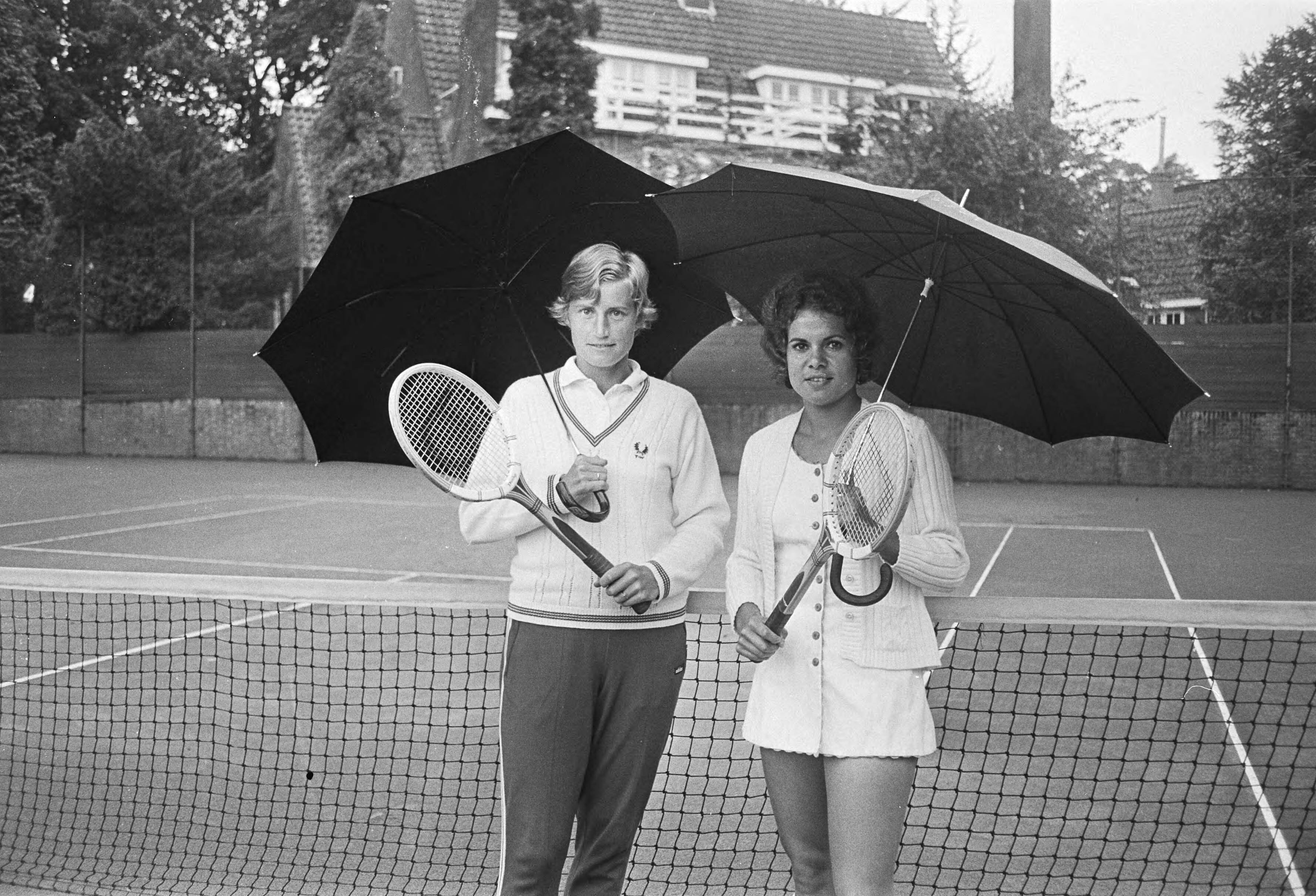 Fotocollectie Anefo — Internationale tenniskampioenschappen in Hilversum, Trudy Walhof en Evonne Goolagong (rechts) onder paraplu — Foto: Peters, Hans / Anefo. Licentie: Set B: Rechtenvrij / Publiek Domein. Bron: Nationaal Archief. http://hdl.handle.net/10648/abc8371a-d0b4-102d-bcf8-003048976d84