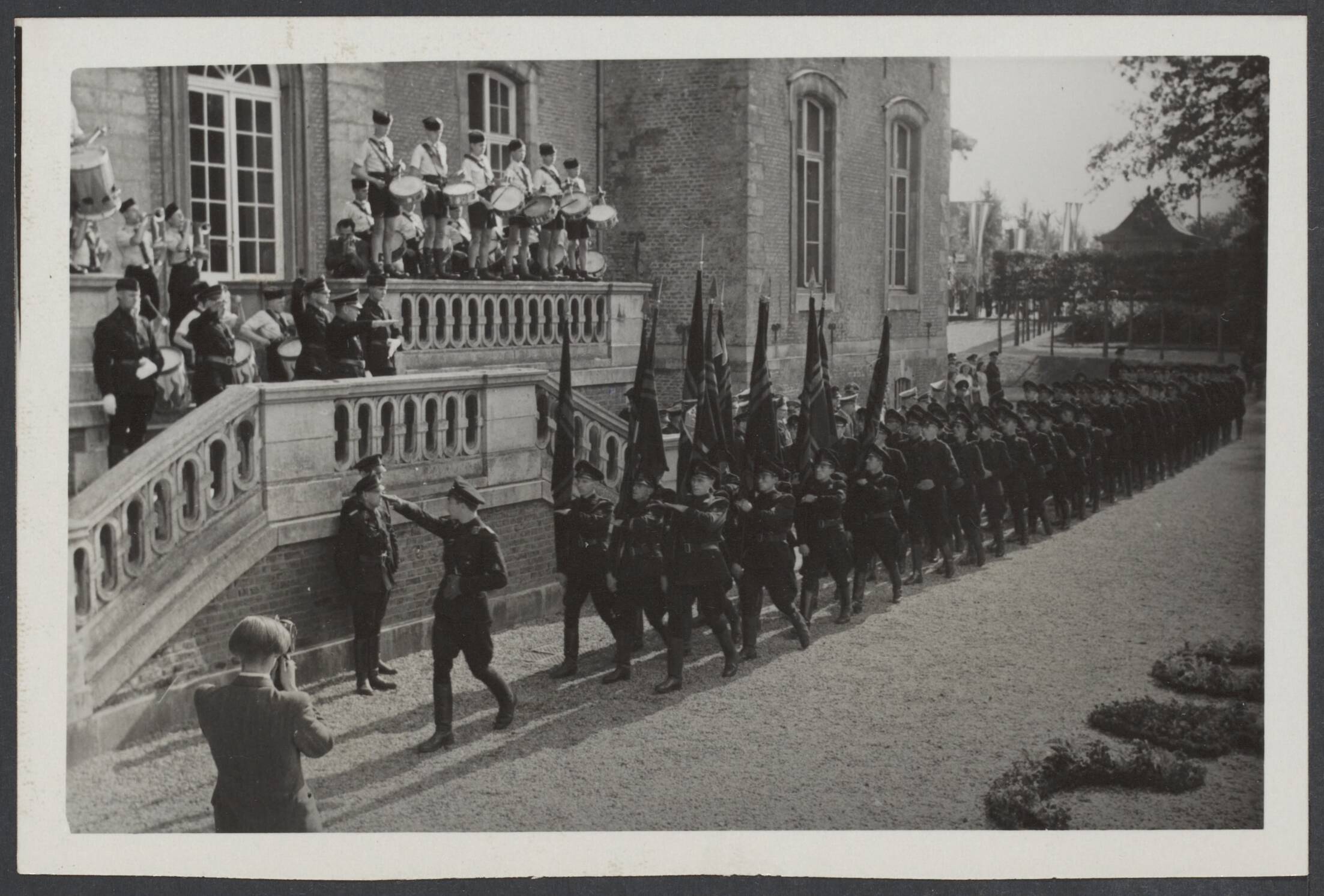 N.S.B. I t/m IX. Nog in te delen. — Heden bracht de leider der NSB, Mussert, tijdens zijn bezoek aan Limburg ook een bezoek aan de Limburgse volksdag, die, de traditiegetrouw, nabij kasteel Amstenrade werd gehouden. Vanaf het bordes van het kasteel Amstenrade werd door de leider der NSB, Mussert, en andere autoriteiten het defilé afgenomen van de WA — Foto: Fotodienst der NSB / N.V. Polygoon. Licentie: Set B: Rechtenvrij / Publiek Domein. Bron: Nationaal Archief. http://hdl.handle.net/10648/91e8626a-636f-9484-e07c-17820cf76125