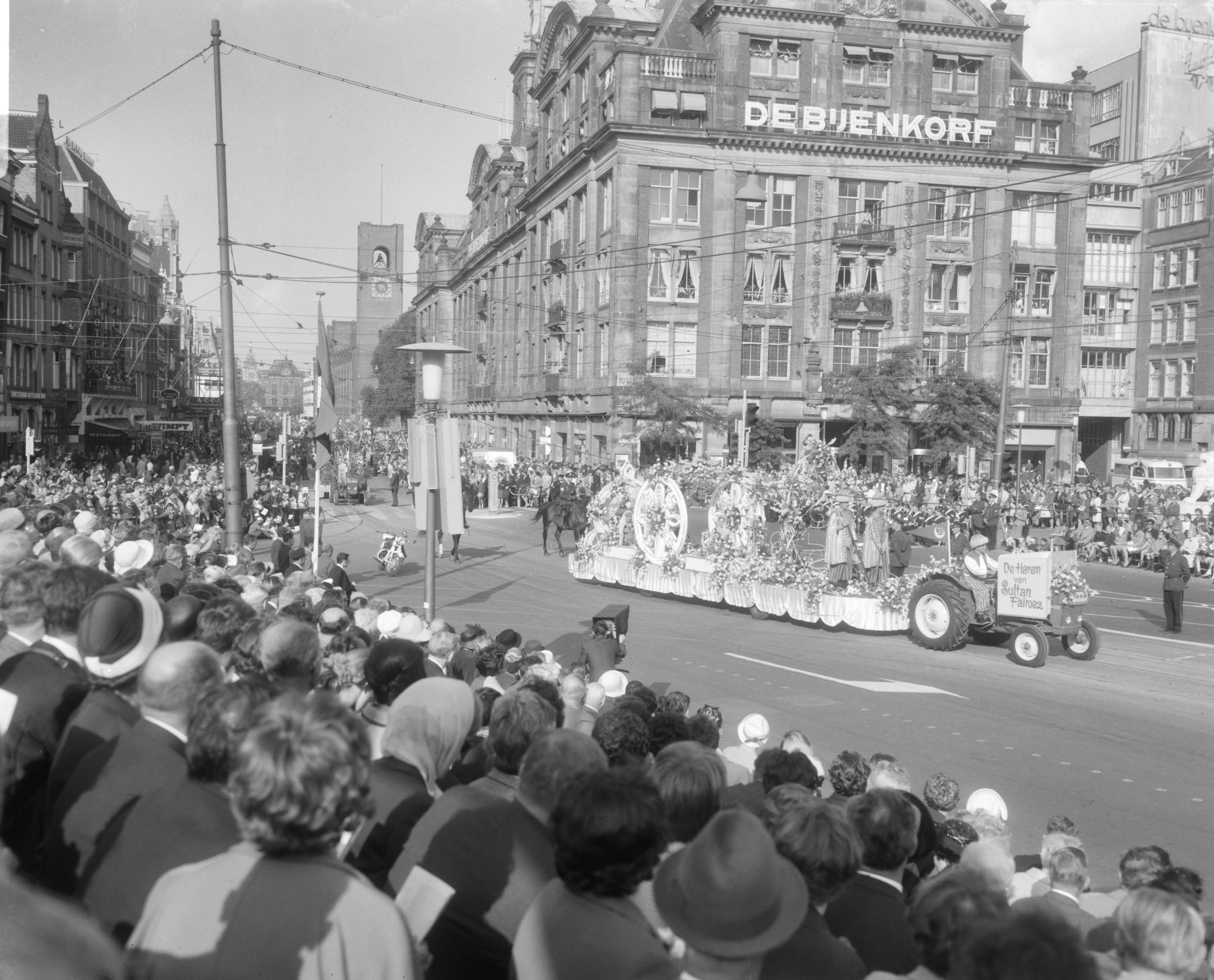 Bloemencorso van Aalsmeer te Amsterdam — Een praalwagen bij de Dam te Amsterdam met op de achtergrond het warenhuis de Bijenkorf — Foto: Bilsen, Joop van / Anefo. Licentie: Set B: Rechtenvrij / Publiek Domein. Bron: Nationaal Archief. http://hdl.handle.net/10648/aafaed28-d0b4-102d-bcf8-003048976d84