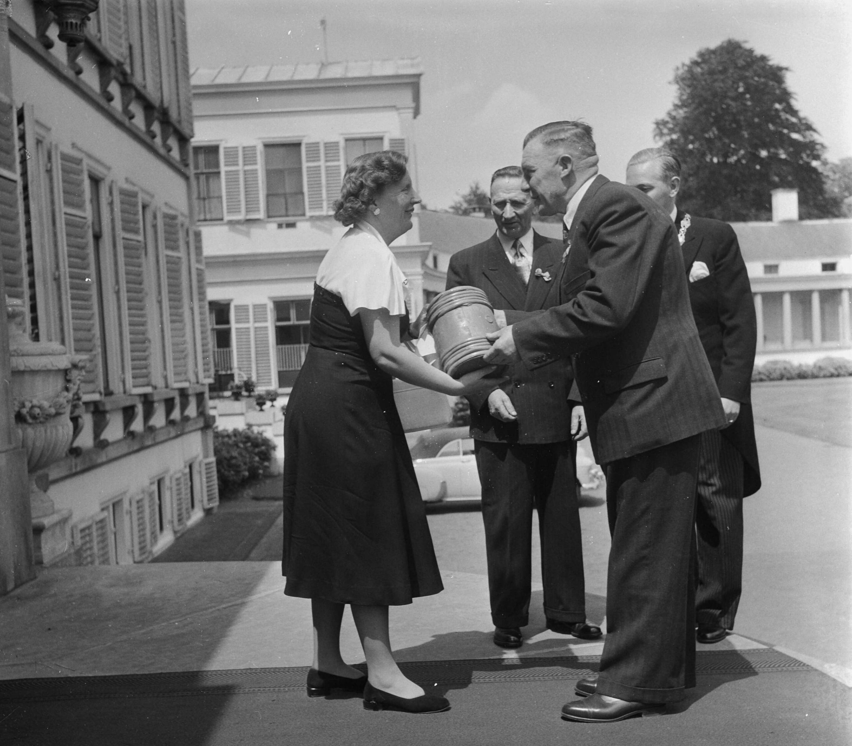 Aanbieding Koninginneharing op Soestdijk — Aanbieding Koninginneharing door de Rijksopperkeurmeester aan koningin Juliana op paleis Soestdijk. Schipper G. van der Snoek van de VL 74 "Hendrika en Adriana" die de haring heeft aangevoerd overhandigt het vaatje aan de koningin. Rechts achter hem de burgemeester van Vlaardingen mr. J. Heusdens. In het midden Rijksopperkeurmeester W. Don — Foto: Noske, J.D. / Anefo. Licentie: Set B: Rechtenvrij / Publiek Domein. Bron: Nationaal Archief. http://hdl.handle.net/10648/a8faedde-d0b4-102d-bcf8-003048976d84