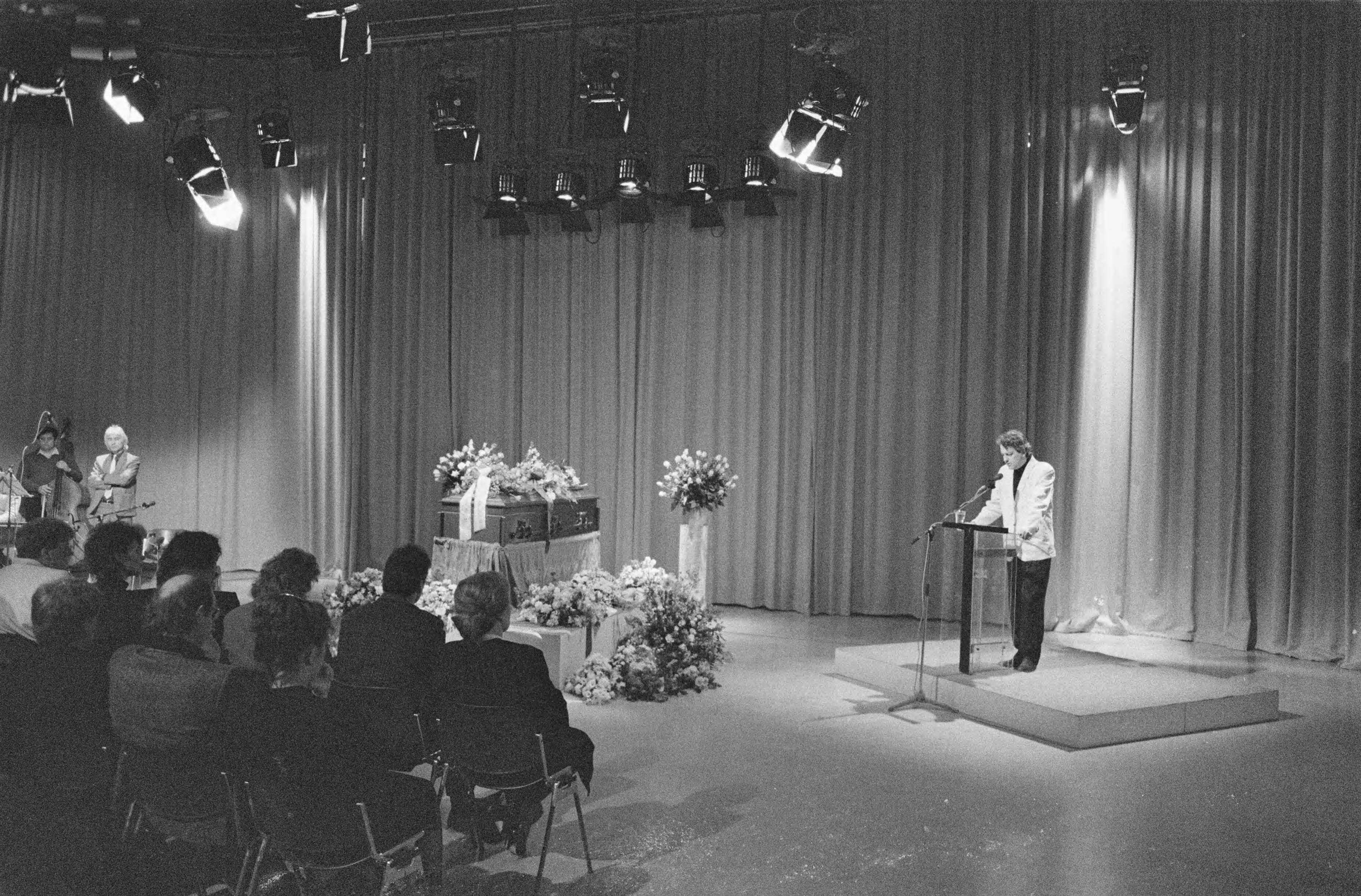 Herdenkingsdienst voor de doodgeschoten cameraman Cornel Lagrouw in Hilversum — Aanwezigen zitten in de ruimte waar de kist met bloemen staat — Foto: Bogaerts, Rob / Anefo. Licentie: Set B: Rechtenvrij / Publiek Domein. Bron: Nationaal Archief. http://hdl.handle.net/10648/ad71d4d6-d0b4-102d-bcf8-003048976d84