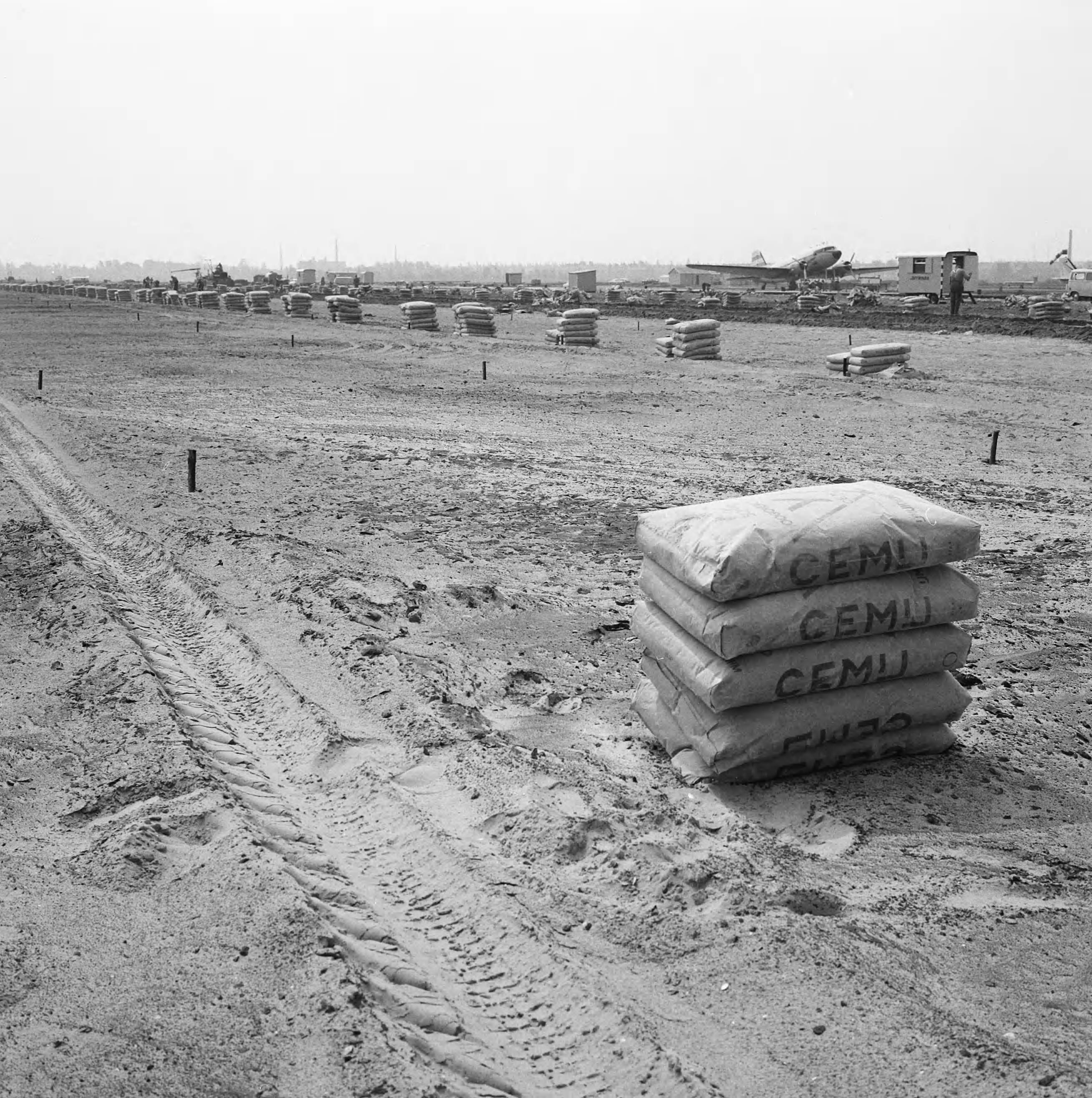 Fotocollectie Nederlandse Heidemaatschappij — Luchthaven Rotterdam. Uitbreiding platform. Fase I en aanleg taxibanen in 1964. Reclame "Cemy"op toekomstig platform — Foto: Wüllschleger, [...] / Heidemij. Licentie: Set B: Rechtenvrij / Publiek Domein. Bron: Nationaal Archief. http://hdl.handle.net/10648/ae7a6a46-d0b4-102d-bcf8-003048976d84