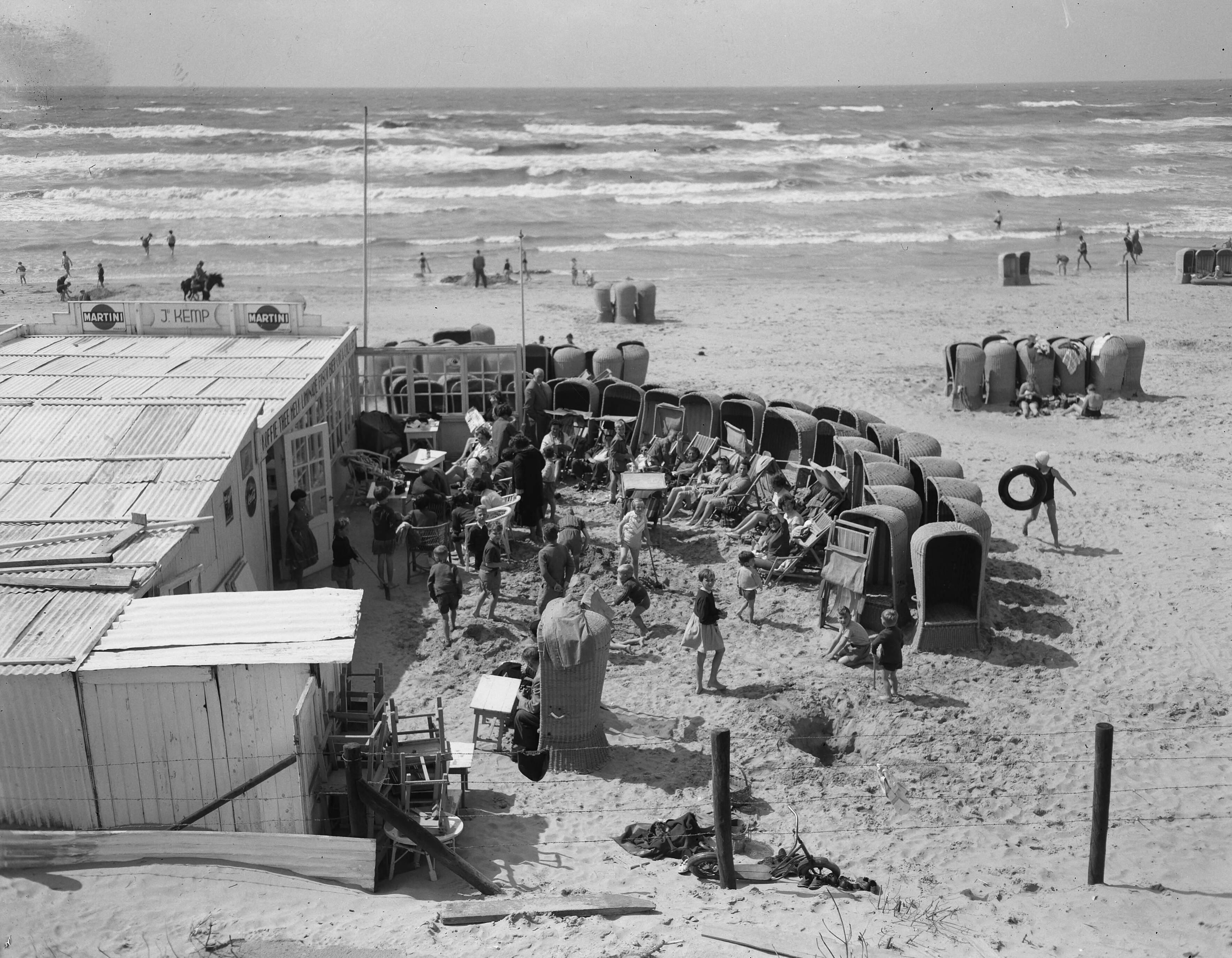 Fotocollectie Anefo — Zandvoort. Slecht strandweer. Strandstoelen staan in een cirkel opgesteld bij een strandpaviloen als bescherming tegen wind — Foto: Noske, J.D. / Anefo. Licentie: Set B: Rechtenvrij / Publiek Domein. Bron: Nationaal Archief. http://hdl.handle.net/10648/a9271b52-d0b4-102d-bcf8-003048976d84