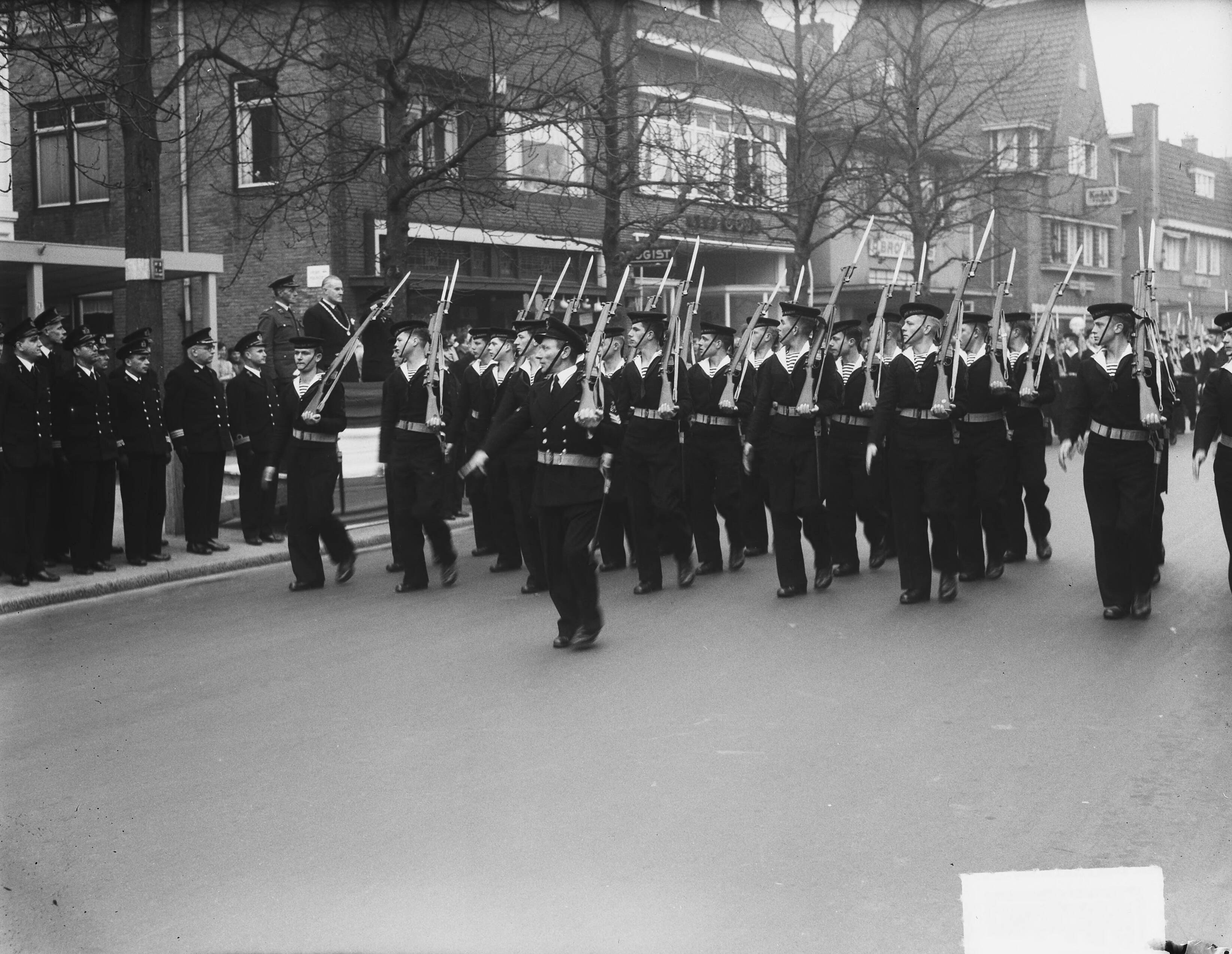 MOK Hilversum 5 jaar defilé en receptie — MOK Hilversum bestaat 5 jaar. Defilé te Hilversum [op een platform voor café De Kerseboom staan vlnr. een luitenant-kolonel van de Koninklijke Landmacht, burgemeester van Hilversum J.A.G.M. van Hellenberg Hubar en de scheidende commandant kapitein-ter-zee S. Dobbinga] — Foto: Vogel, Carel L. de / Anefo. Licentie: Set B: Rechtenvrij / Publiek Domein. Bron: Nationaal Archief. http://hdl.handle.net/10648/a8e6df1a-d0b4-102d-bcf8-003048976d84
