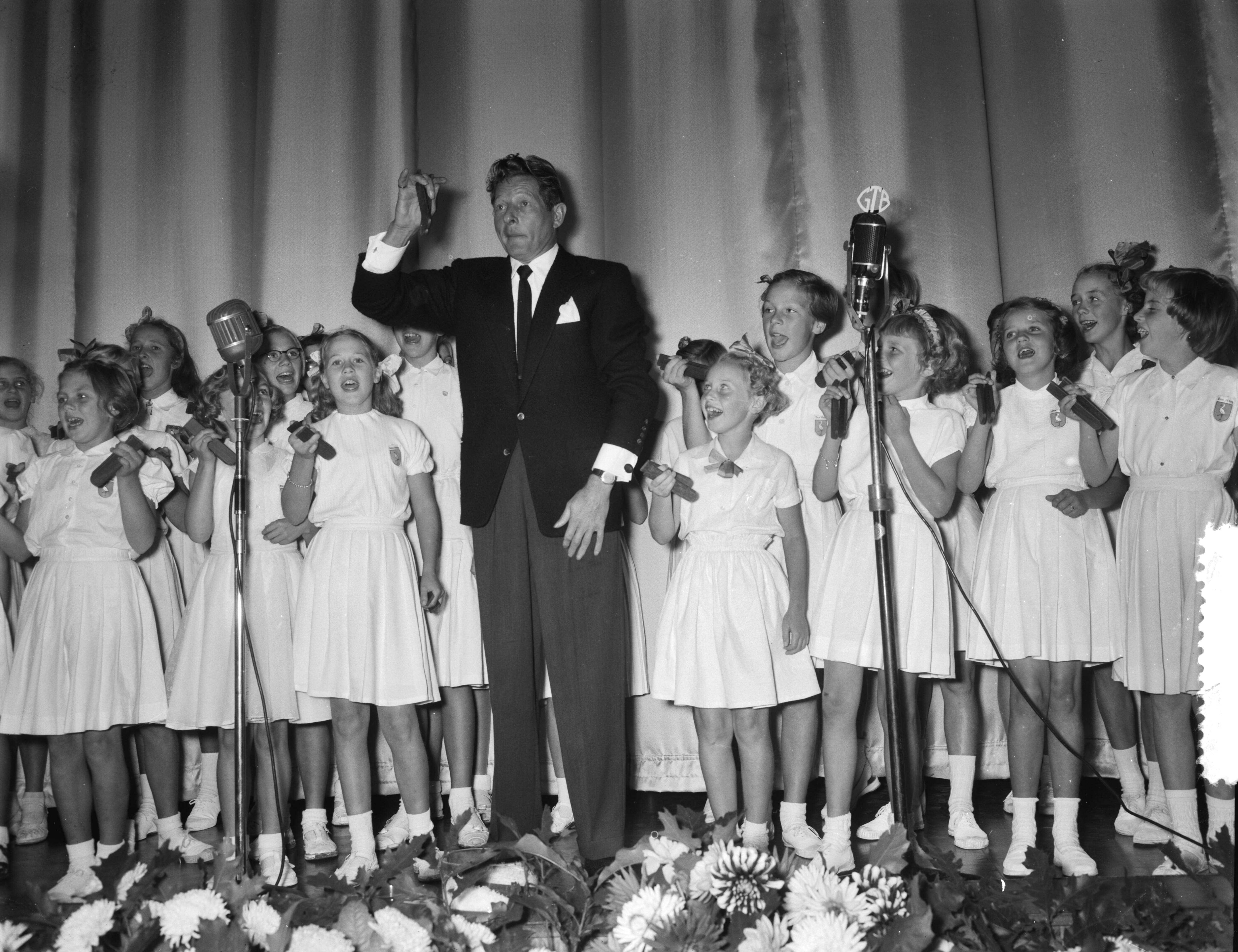 Fotocollectie Anefo — Première van de UNICEF-film "Kinderogen lachen weer" in het Metropole-Tuschinski theater te Den Haag. Danny Kaye kleppert met het kinderkoor "De Haagse Ooievaartjes" — Foto: Noske, J.D. / Anefo. Licentie: Set B: Rechtenvrij / Publiek Domein. Bron: Nationaal Archief. http://hdl.handle.net/10648/a93c56d4-d0b4-102d-bcf8-003048976d84
