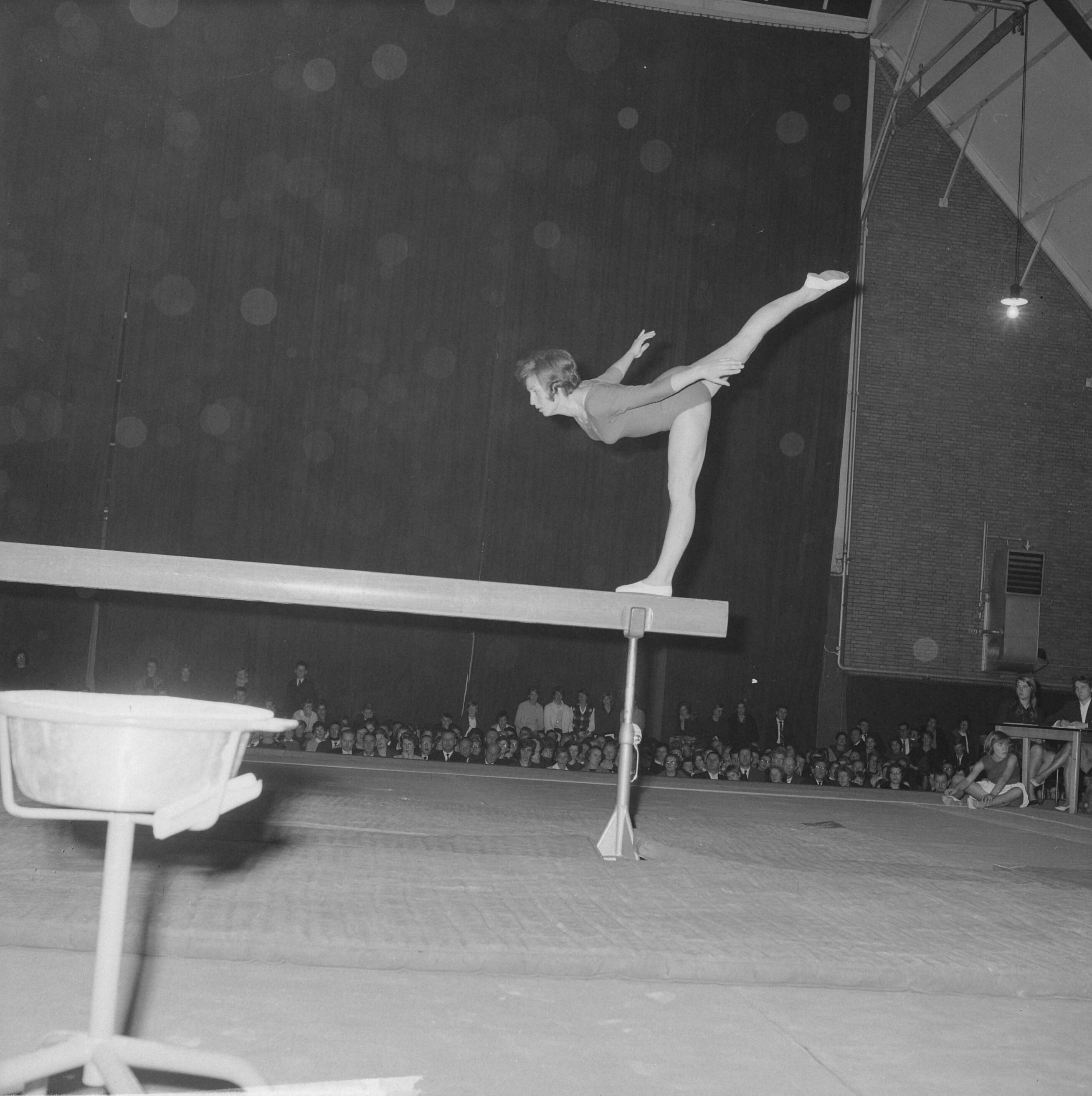 Fotocollectie Anefo — Turninterland Nederland-West-Duitsland in de Centrale Veilinghal te Aalsmeer. Turnster op evenwichtsbalk — Foto: Nijs, Jac. de / Anefo. Licentie: Set B: Rechtenvrij / Publiek Domein. Bron: Nationaal Archief. http://hdl.handle.net/10648/aa20053c-d0b4-102d-bcf8-003048976d84