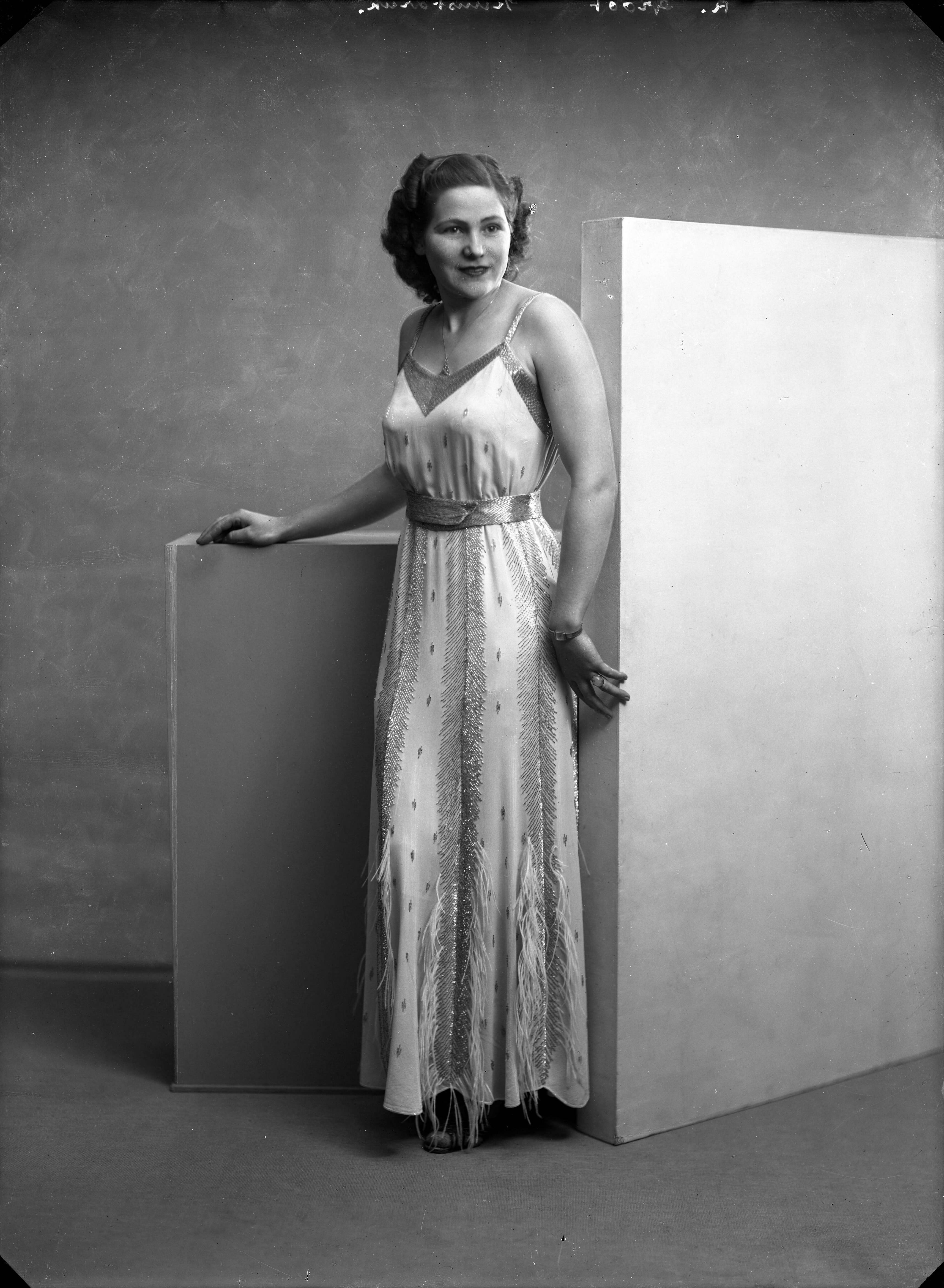 Berg, van den (BERG 050) — Studio-opnames. Een vrouw in een lange satijnen v-halsjurk met spaghettibandjes versierd met een zilverdraadmotief. R. Groot kunstdruk. Haarlem, Nederland. 1918-1930. — Foto: Berg, Th.C.J. van den / Spaarnestad Photo (05887). Licentie: Set B: Rechtenvrij / Publiek Domein. Bron: Nationaal Archief. http://hdl.handle.net/10648/35429da7-c556-a382-e063-6df0900a6686