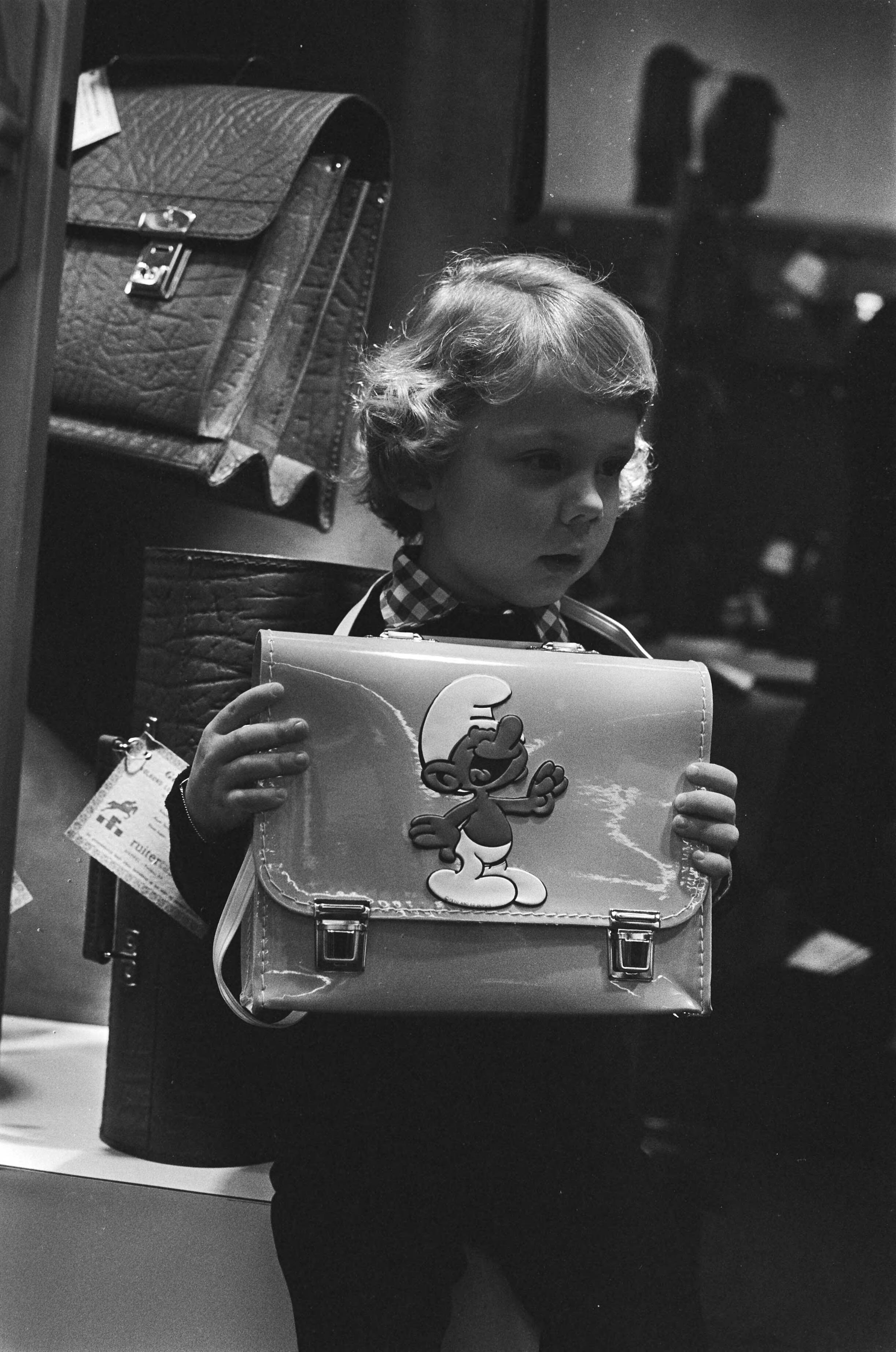 Fotocollectie Anefo — Wintervakbeurs voor koffers en lederwaren in Jaarbeurs Utrecht; schooltas met smurfje — Foto: Bogaerts, Rob / Anefo. Licentie: Set B: Rechtenvrij / Publiek Domein. Bron: Nationaal Archief. http://hdl.handle.net/10648/aca9be10-d0b4-102d-bcf8-003048976d84
