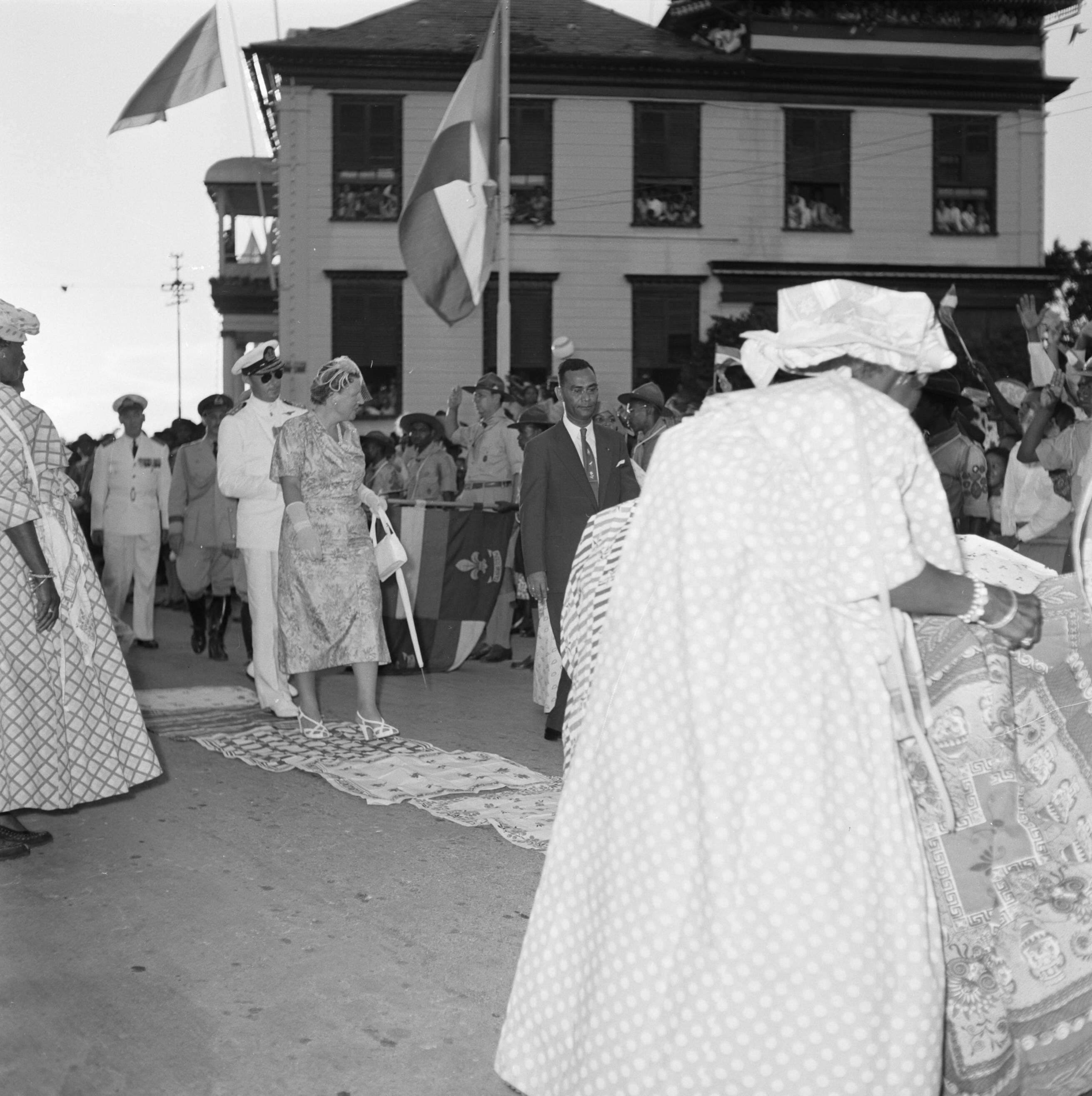 Nederlandse Antillen en Suriname ten tijde van het koninklijk bezoek van koningin Juliana en prins Bernhard in 1955 — De koningin loopt door Domburg. Op de voorgrond een kotomisi — Foto: Poll, Willem van de. Licentie: Set B: Rechtenvrij / Publiek Domein. Bron: Nationaal Archief. http://hdl.handle.net/10648/aeb265a4-d0b4-102d-bcf8-003048976d84
