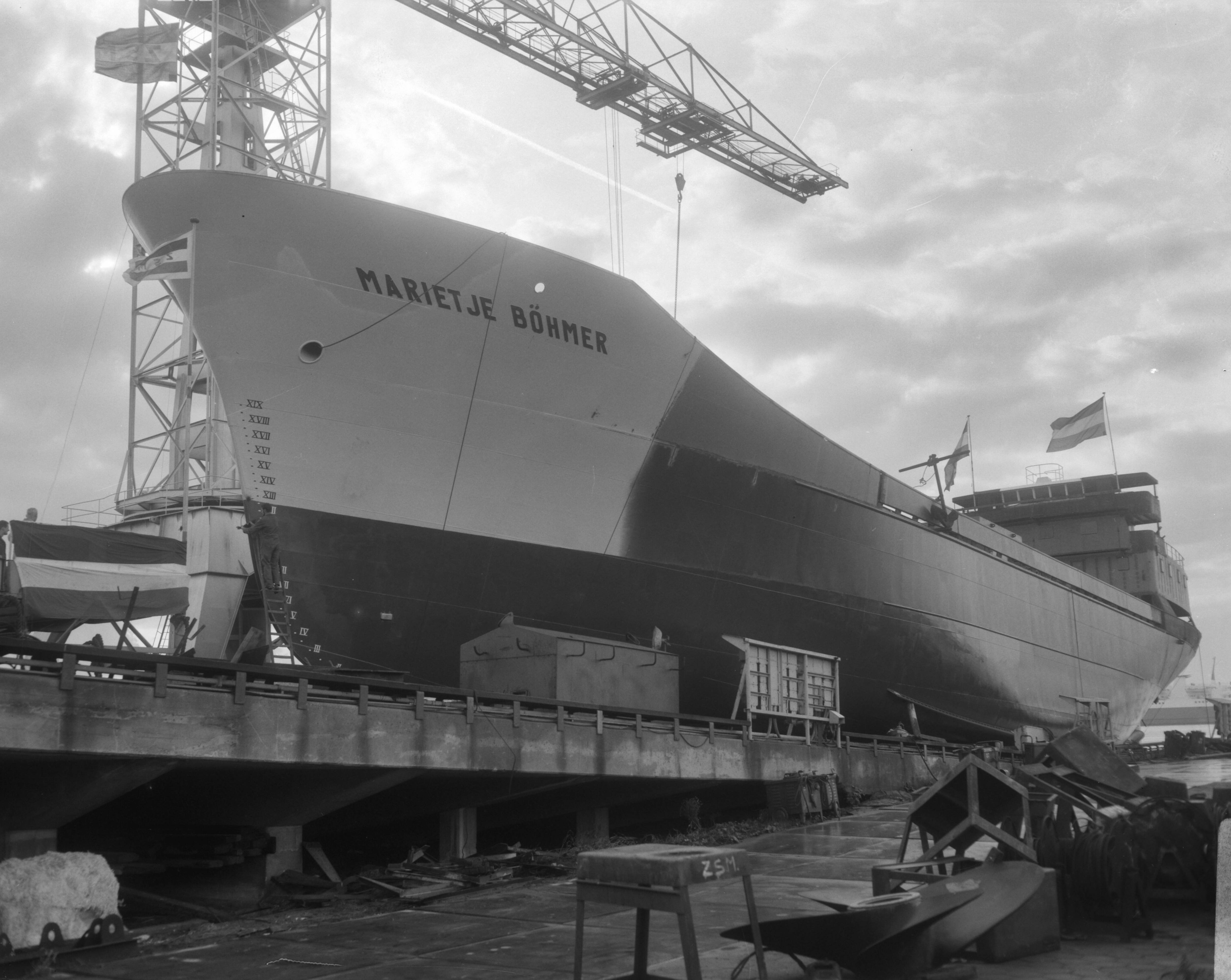 Tewaterlating van de motorcoaster Marietje Böhmer op de scheepswerf Achtersluispolder van de Zaanlandse Scheepsbouw Maatschappij Z.S.M. — Zaanstad|Noord-Holland|tewaterlatingen |scheepsbouw — Foto: Bilsen, Joop van / Anefo. Licentie: Set B: Rechtenvrij / Publiek Domein. Bron: Nationaal Archief. http://hdl.handle.net/10648/ab026fe4-d0b4-102d-bcf8-003048976d84